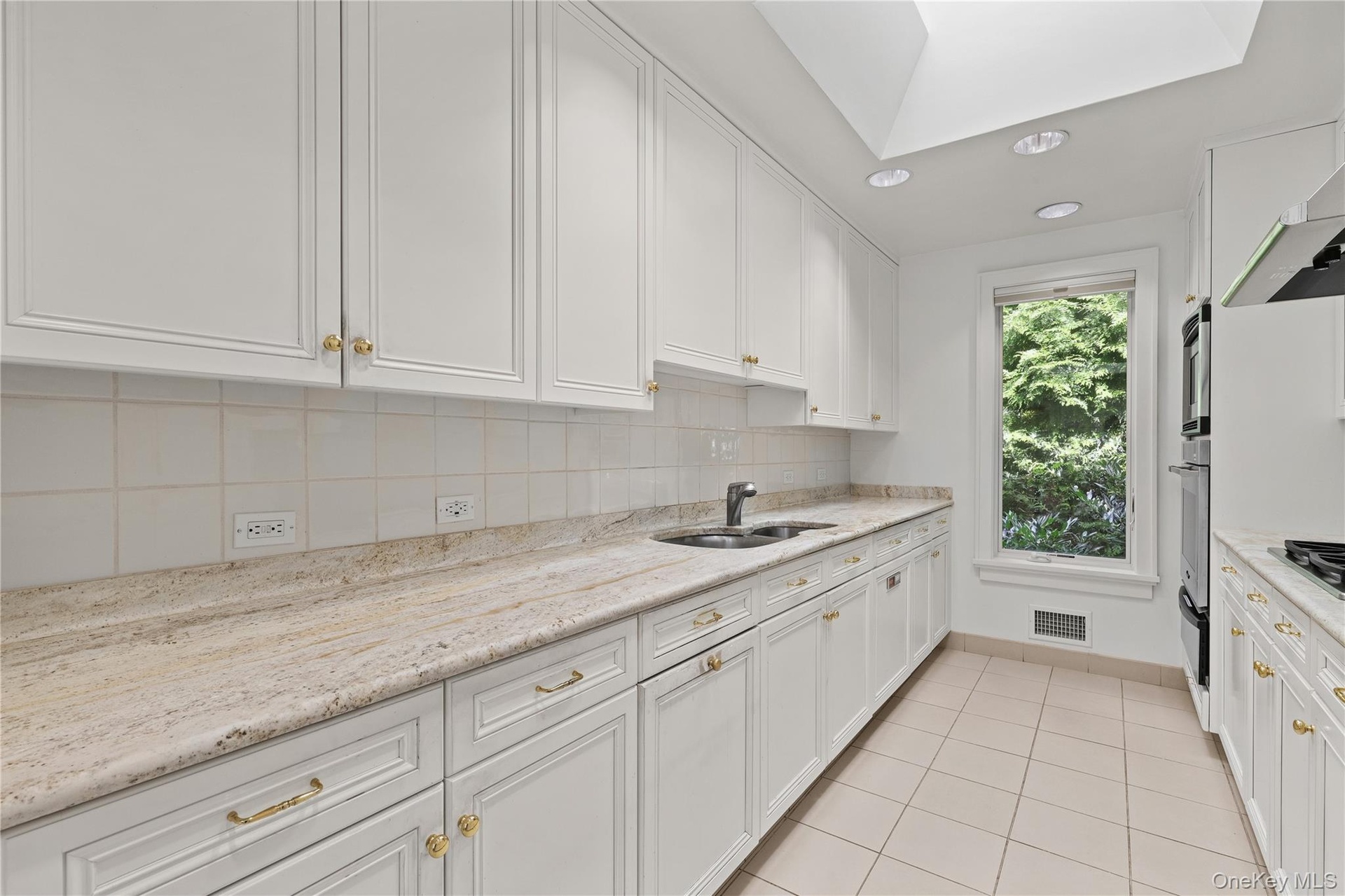 Kitchen featuring white cabinetry, stone countertops, integrated double wall ovens, recessed lighting, and a skylight