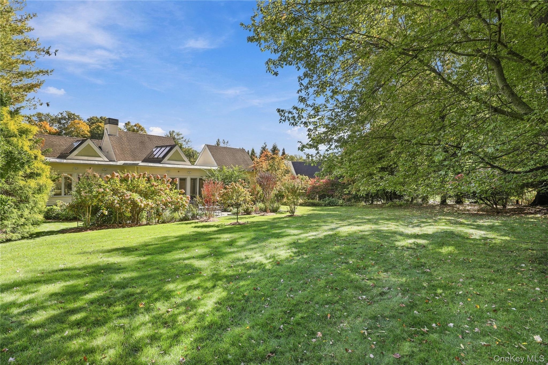 Expansive rear lawn featuring mature shade trees, extensive landscaping, and multi-gabled roofline