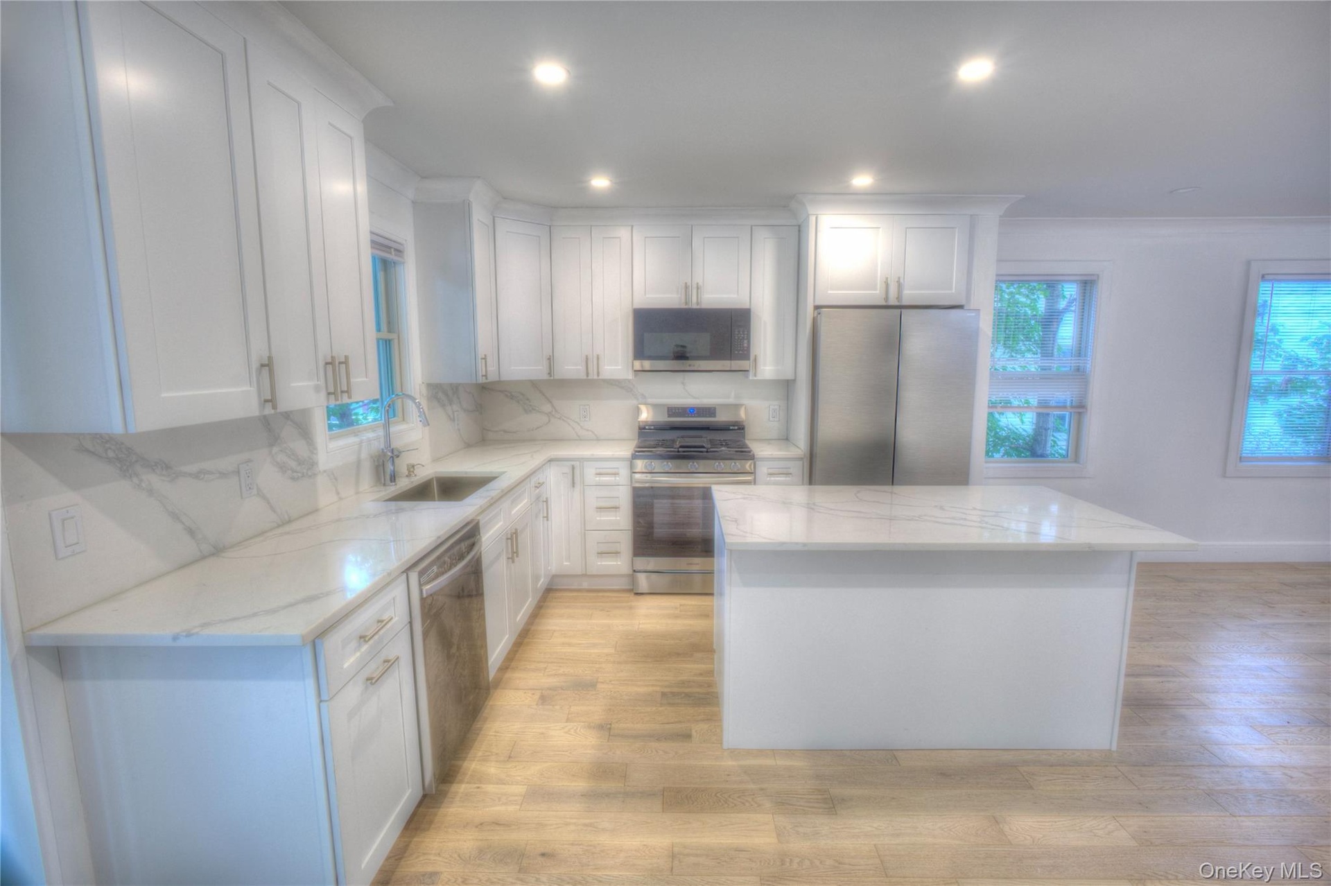 Kitchen featuring white shaker-style cabinetry, stone-finish countertops with integrated backsplash, a central island, stainless steel appliances, and