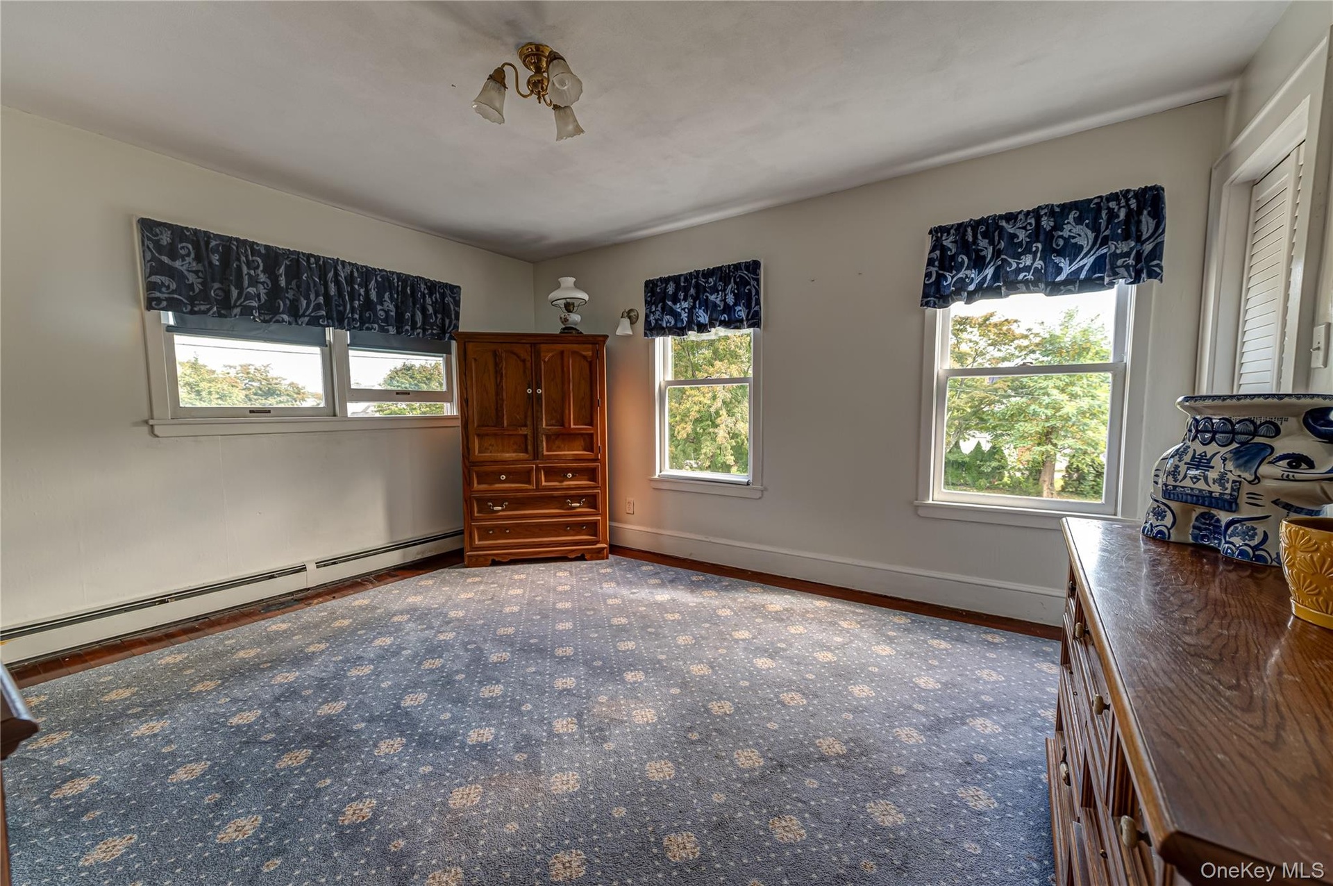 Generously sized primary bedroom on second floor featuring three double-pane windows, neutral wall paint, hardwood floors and a ceiling-mounted light 