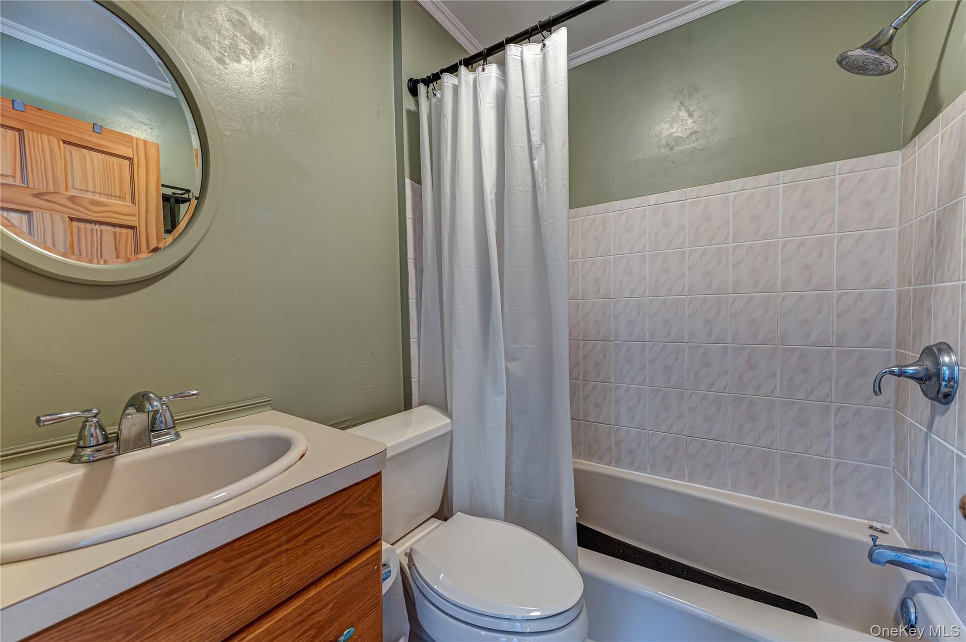Bathroom featuring a wood-finish vanity, integrated sink, circular wall-mounted mirror, and a tile-surround shower and tub combination