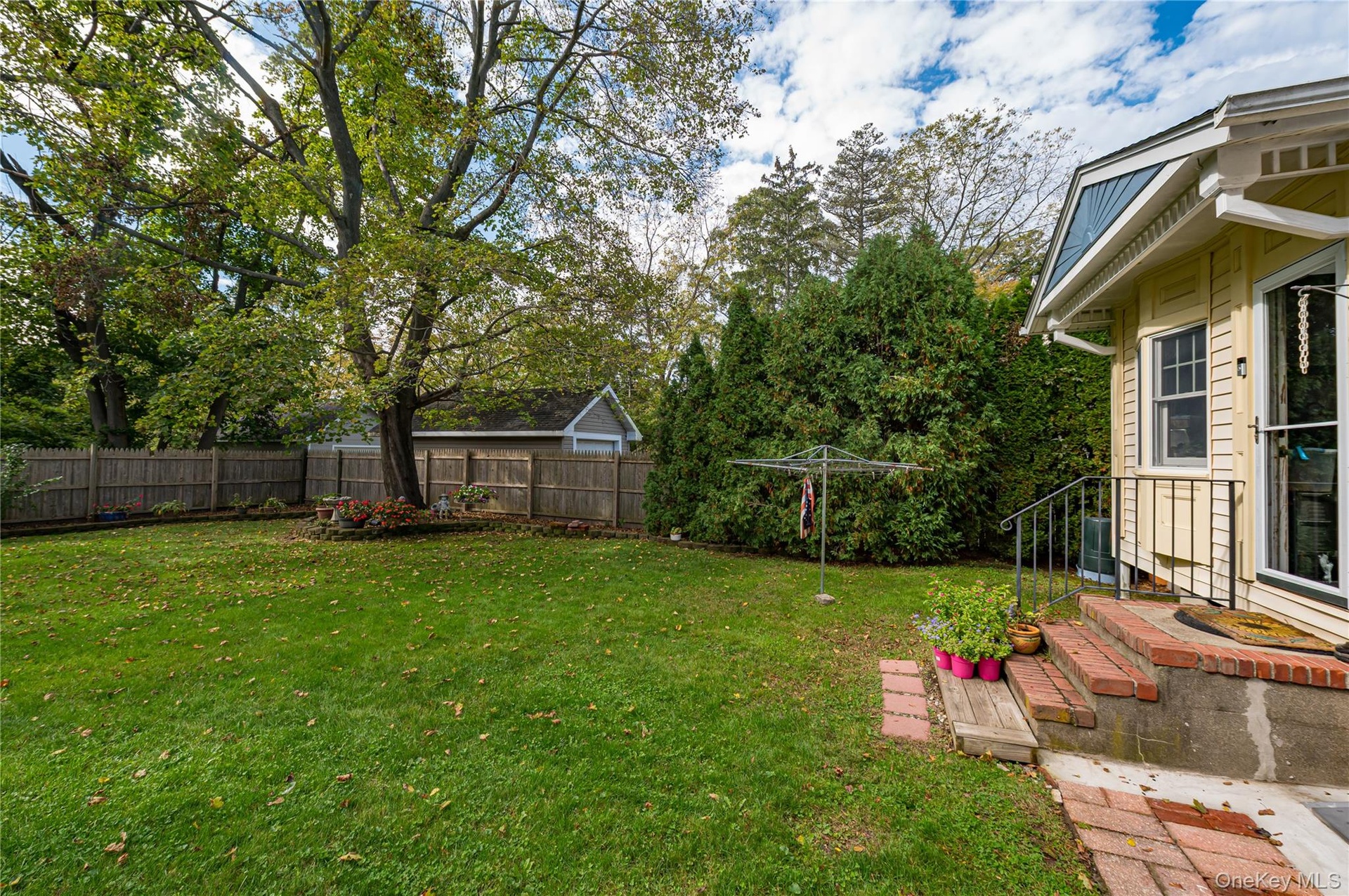 Private backyard featuring a level lawn, mature trees, wood privacy fencing, and a brick-stepped entrance