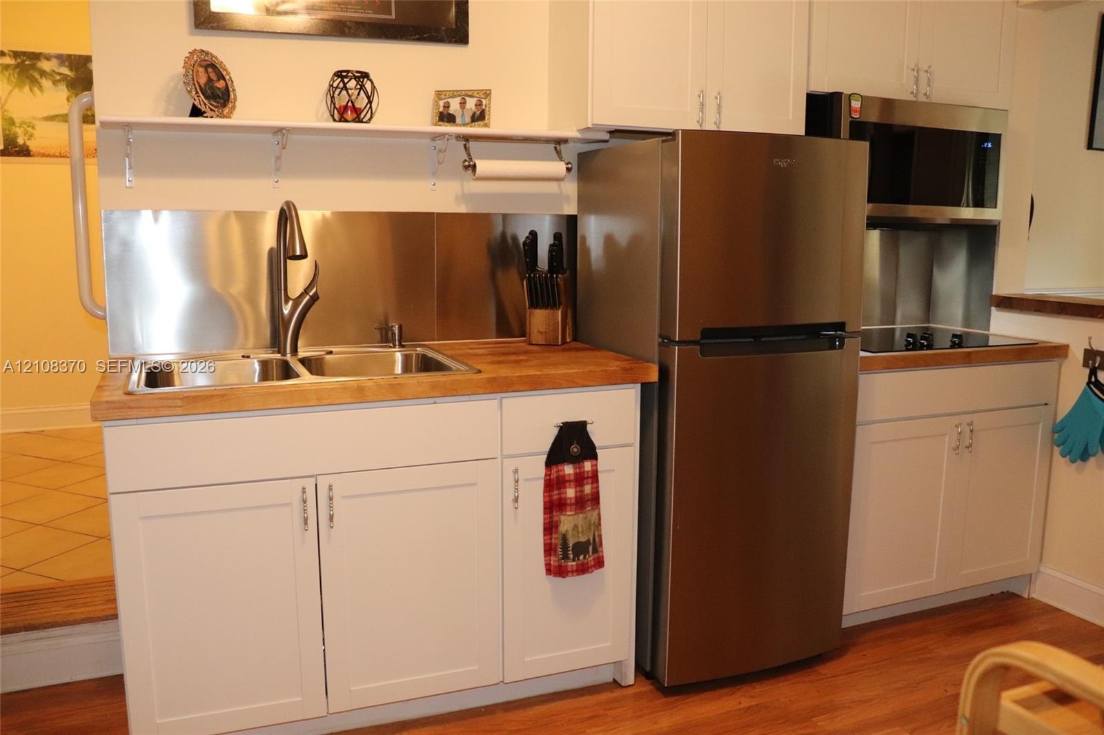 White shaker-style cabinetry, wood-surface countertops, stainless steel appliances, dual-basin stainless steel sink with high-arc faucet, and stainles