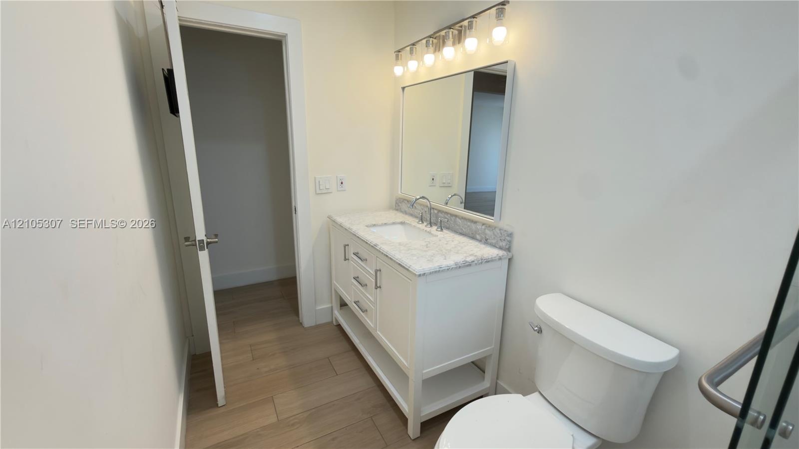 Bathroom vanity featuring stone-finish countertop, integrated sink, and white cabinetry, accompanied by a rectangular mirror, five-light fixture, and 