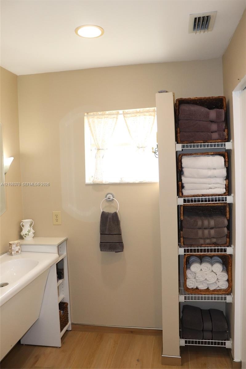 Built-in white vanity with integrated basin, light-toned wood-finish flooring, and floor-to-ceiling white wire shelving