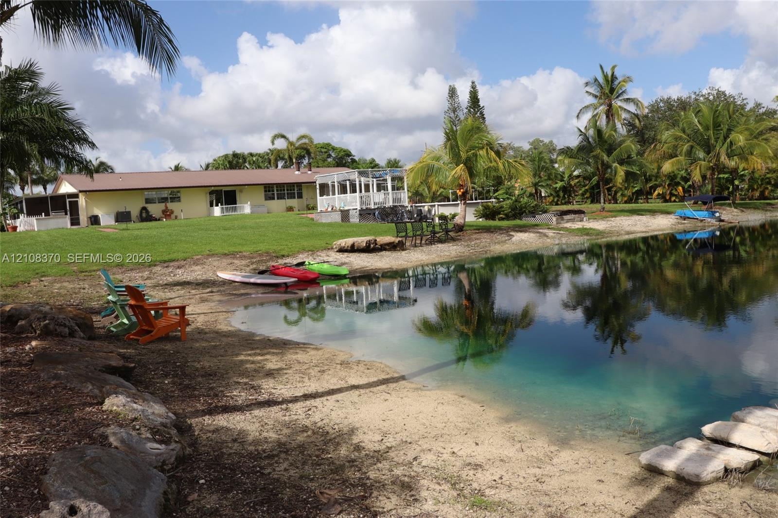 Waterfront property featuring a private sandy shoreline, rock-lined banks, expansive lawn, and an elevated screened enclosure