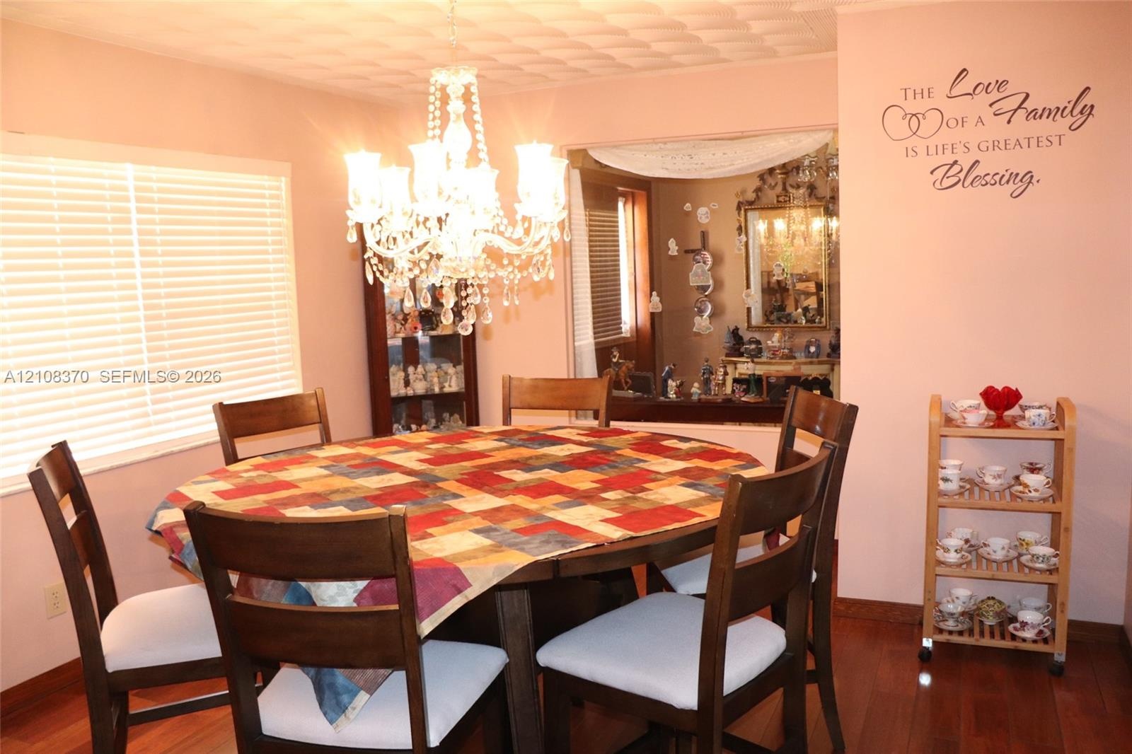 Dining area featuring wood-finish flooring, a multi-tiered crystal chandelier, and large window with horizontal blinds