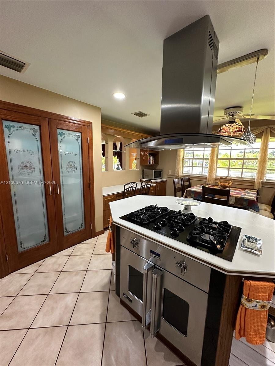 Kitchen featuring a center island with a built-in stainless steel gas cooktop, overhead stainless steel vent hood, pantry with decorative glass-panel 