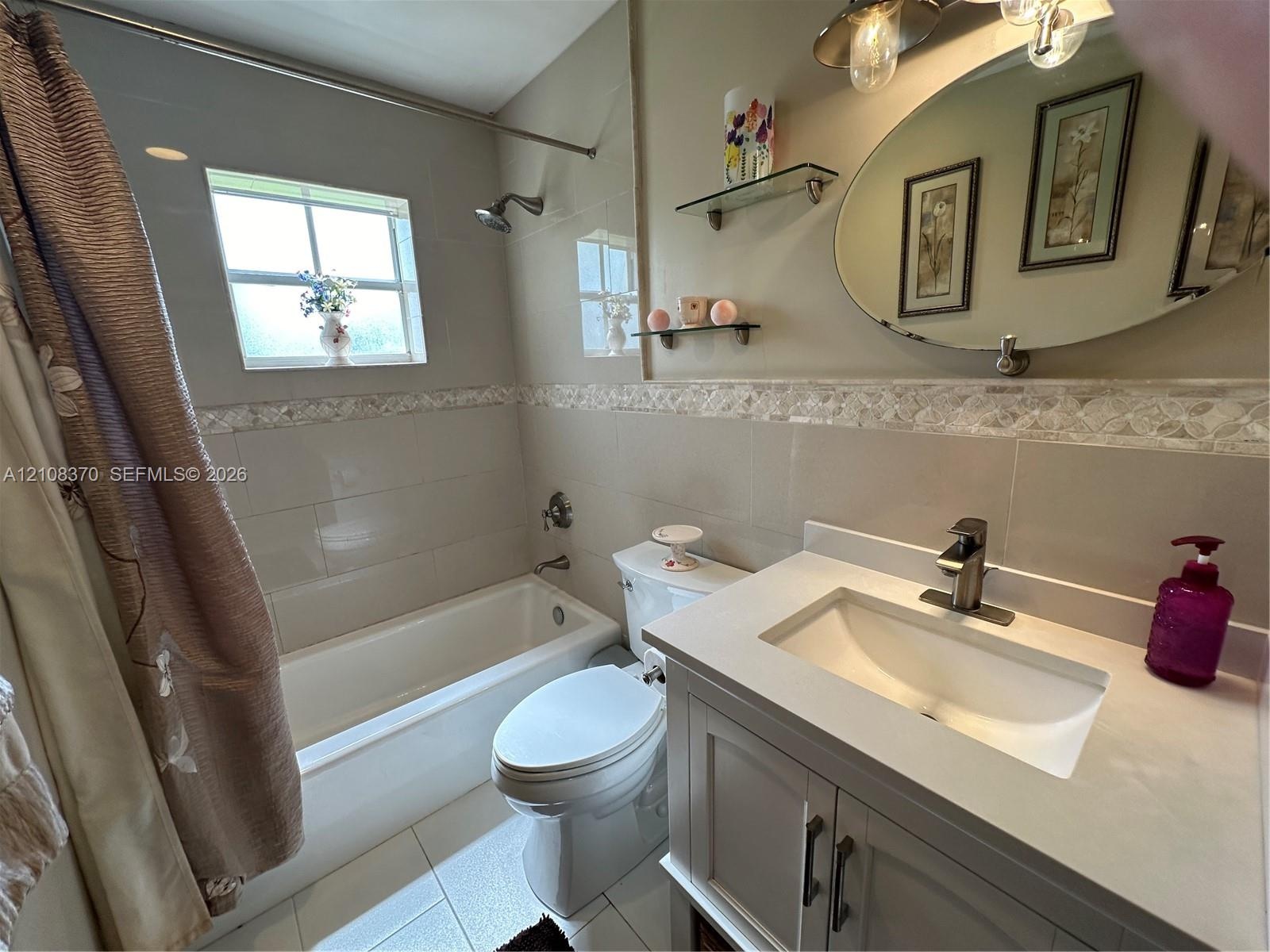Bathroom featuring a vanity with a solid-surface countertop, an integrated sink, an oval wall-mounted mirror, neutral tile wall surround with decorati
