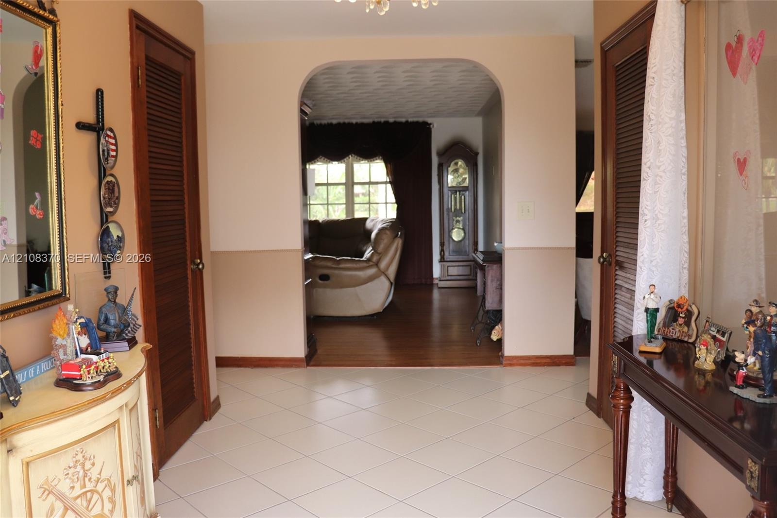 Foyer featuring light-toned tile flooring, a prominent arched entry, wood-finish flooring, and two wooden louvered doors