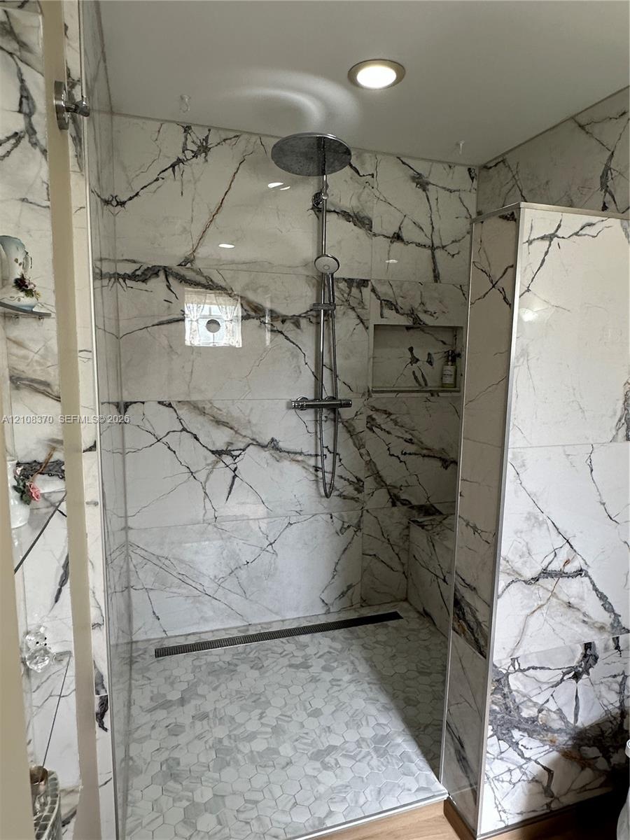 Walk-in shower featuring large-format veined tile surround, recessed wall niche, rain-style shower head, linear floor drain, and hexagonal tile floori