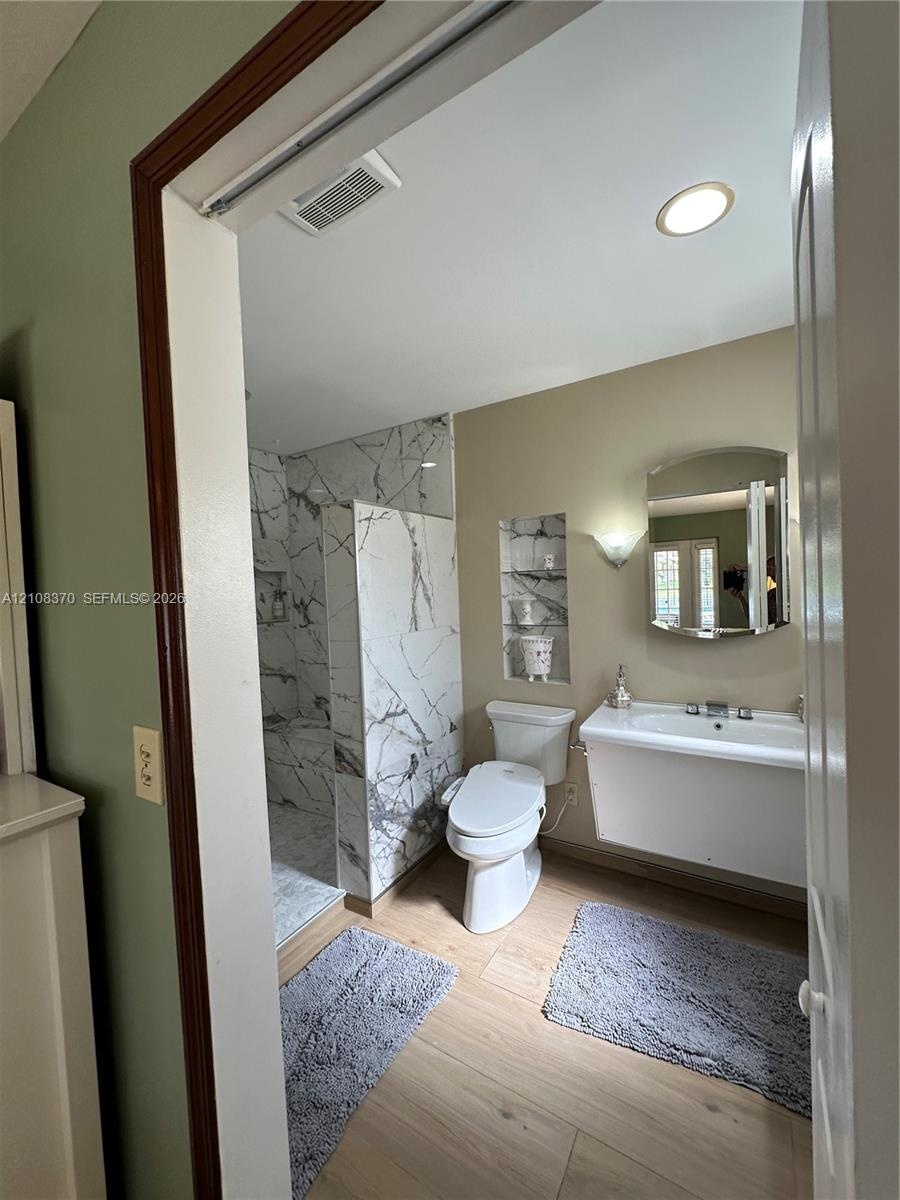 Walk-in shower with floor-to-ceiling veined tile surround, recessed wall shelving, wall-mounted vanity, and wood-finish flooring