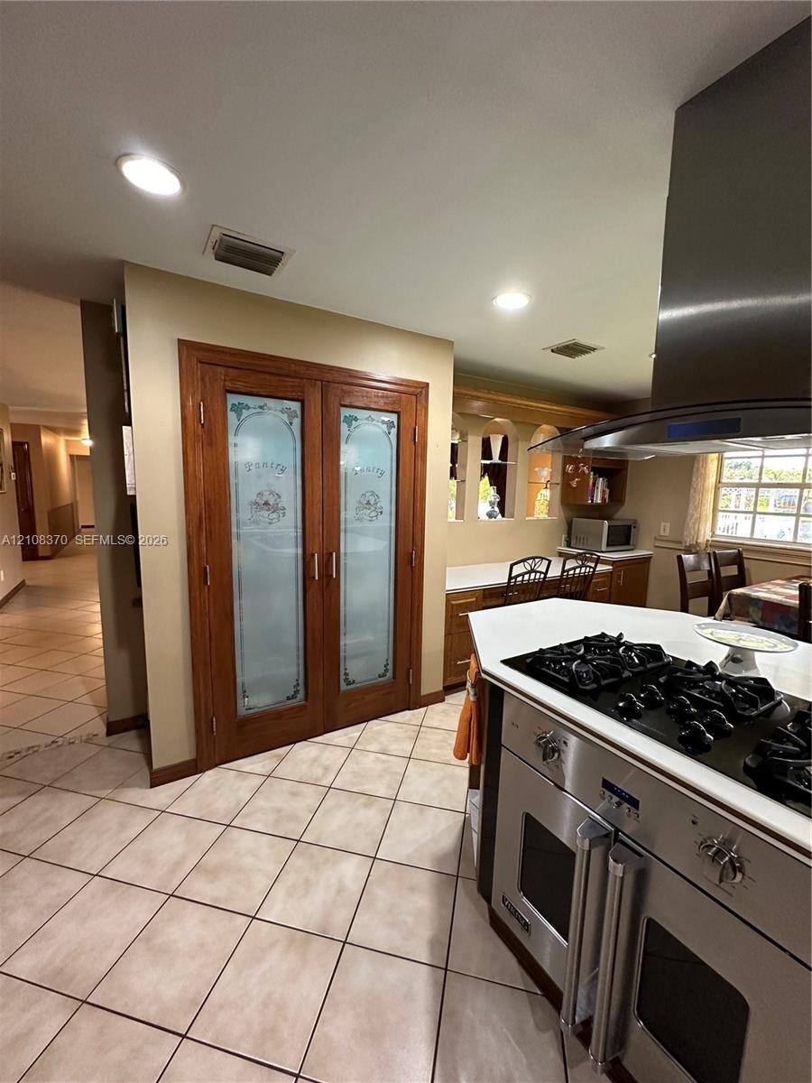 Double pantry with frosted glass paneled doors, stainless steel gas range with overhead ventilation hood, recessed lighting, and tile flooring