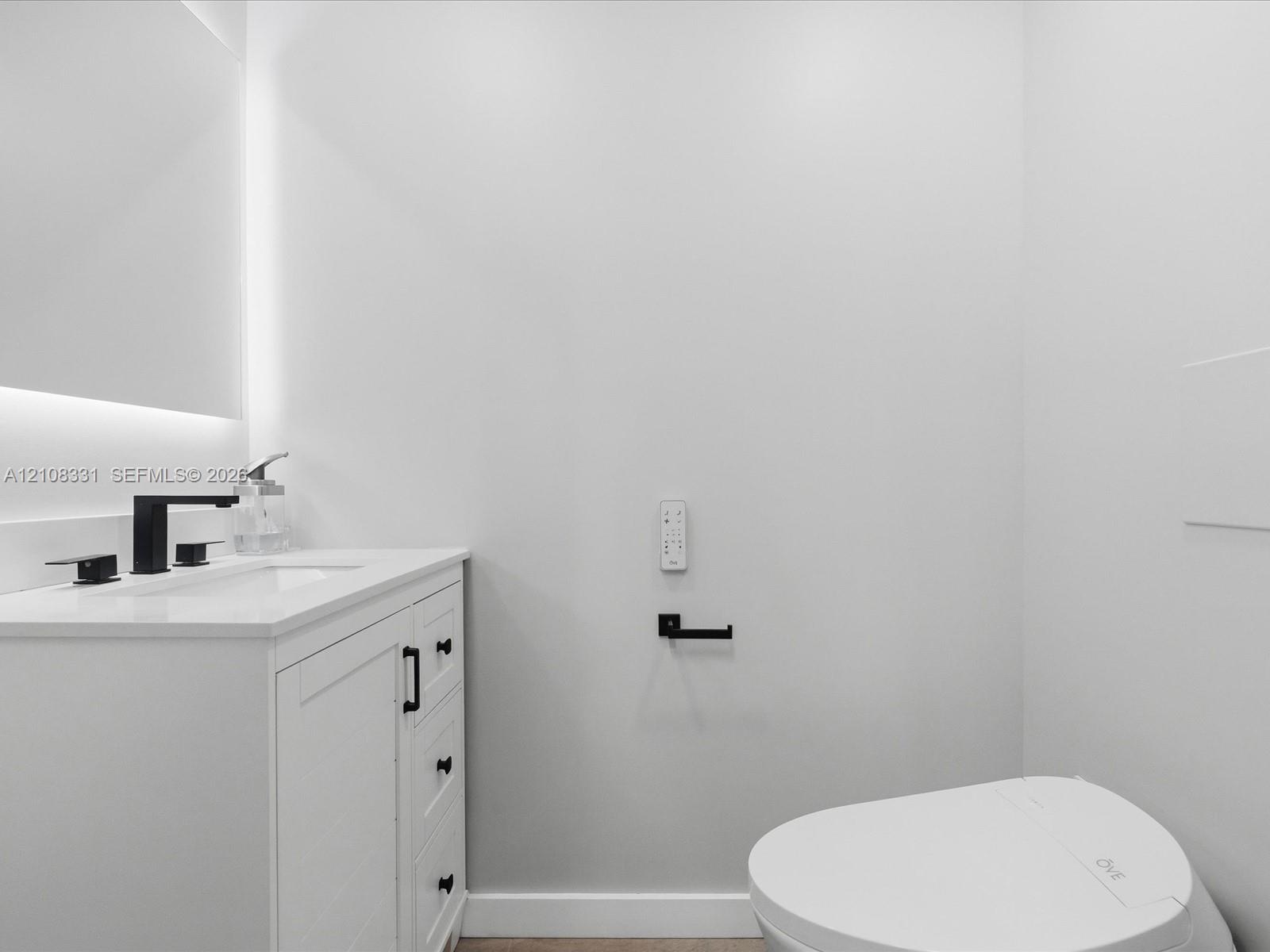 White shaker-style vanity with stone-composite countertop, integrated sink, matte black widespread faucet, and integrated backlighting
