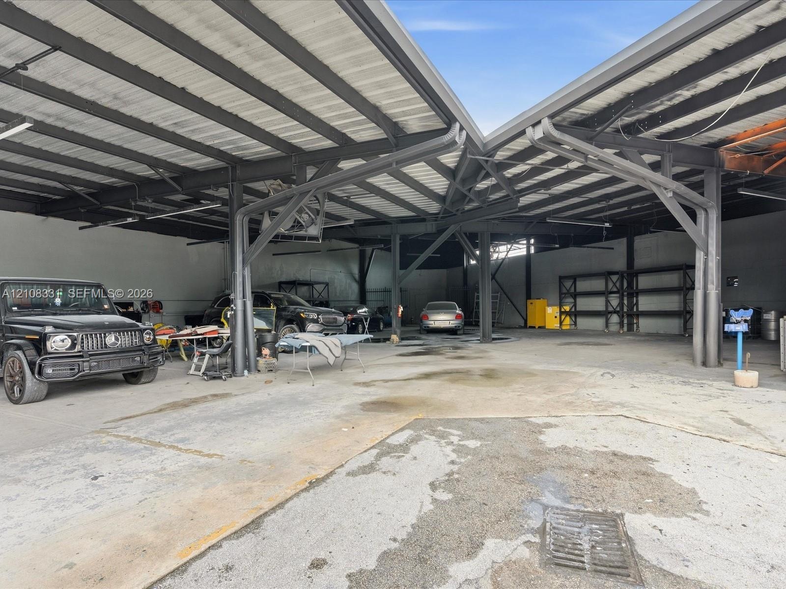 Expansive covered workspace featuring high-clearance steel beam construction, corrugated metal roofing, integrated ceiling-mounted lighting, and concr