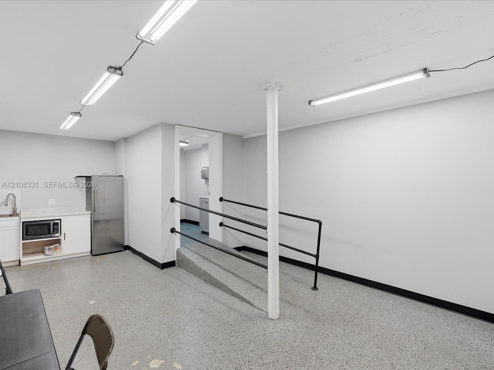 Open interior space featuring speckled flooring, built-in cabinetry with a stone-surface countertop, stainless steel refrigerator, and metal handrails