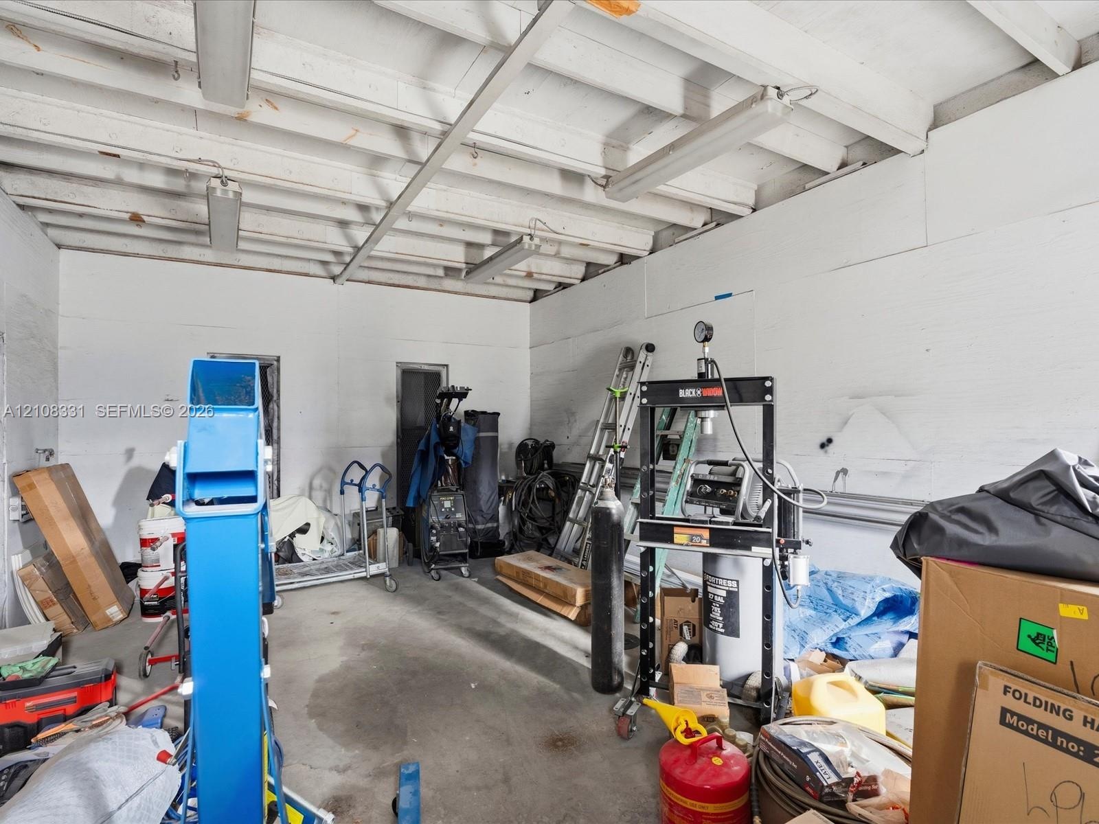 Garage space featuring exposed beam ceiling, concrete flooring, and linear fluorescent overhead lighting