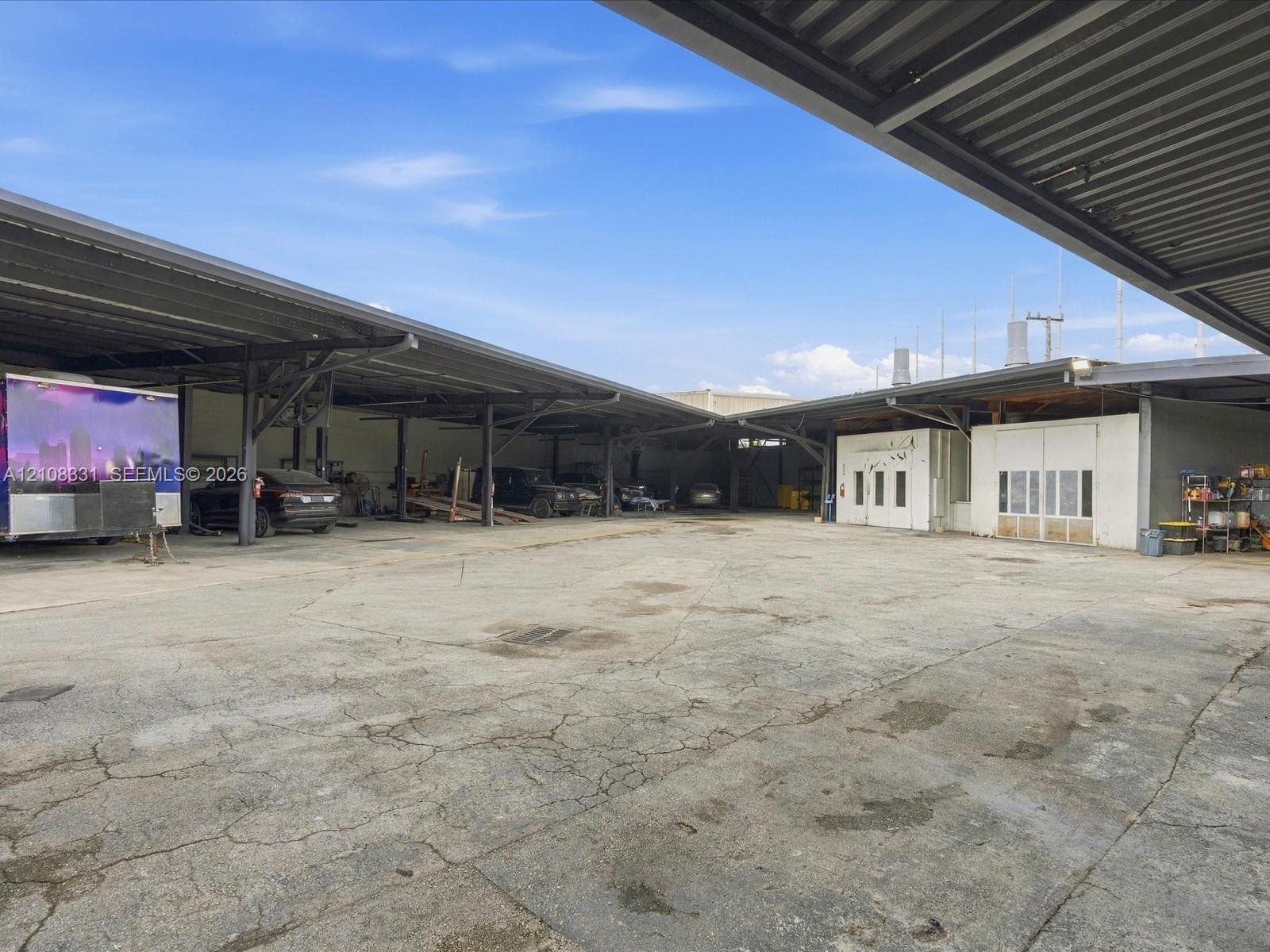 Expansive industrial property featuring a large concrete lot and extensive covered parking structure supported by steel beams