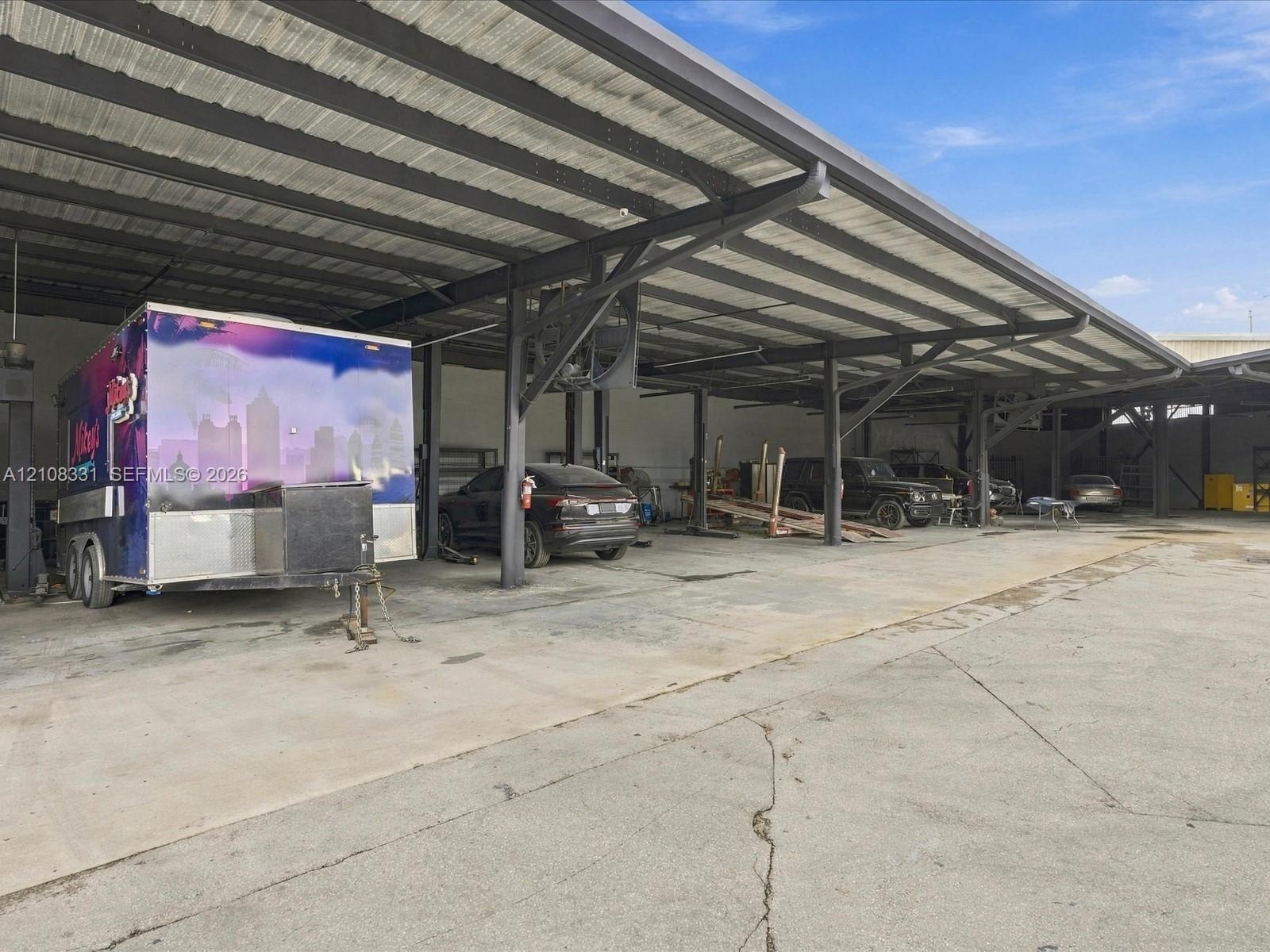 Expansive industrial-style covered parking area featuring a high-clearance metal roof, steel structural support beams, and a concrete slab foundation