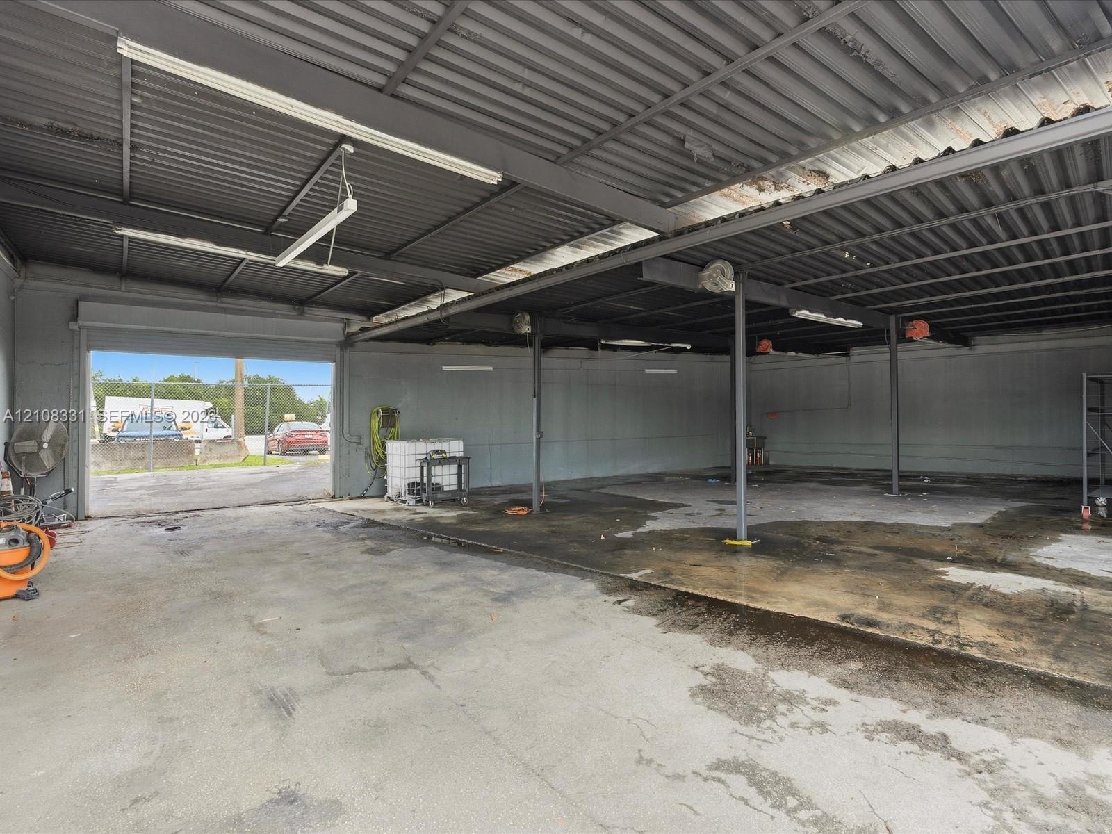 Open-concept warehouse space featuring high-clearance metal corrugated roofing, concrete flooring, support columns, and a large roll-up entry door