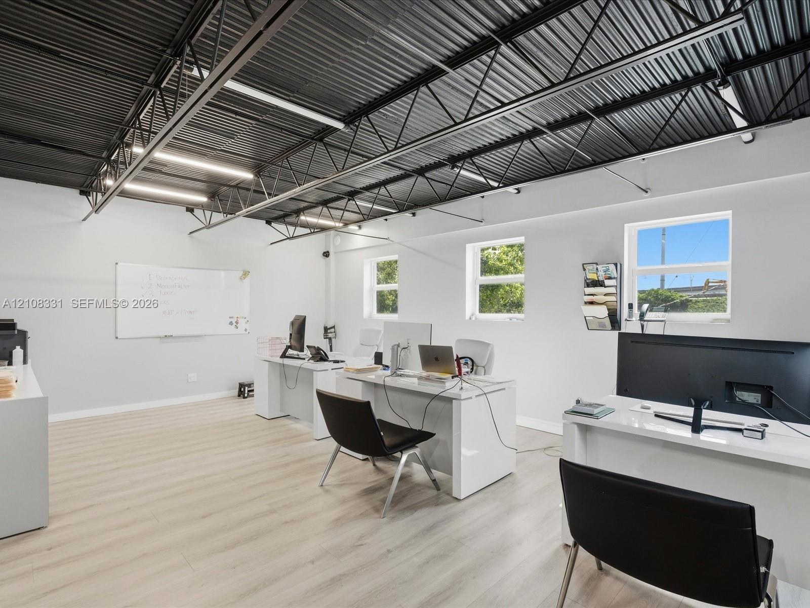 Open-concept space featuring wood-finish flooring, exposed industrial ceiling trusses, and recessed linear lighting