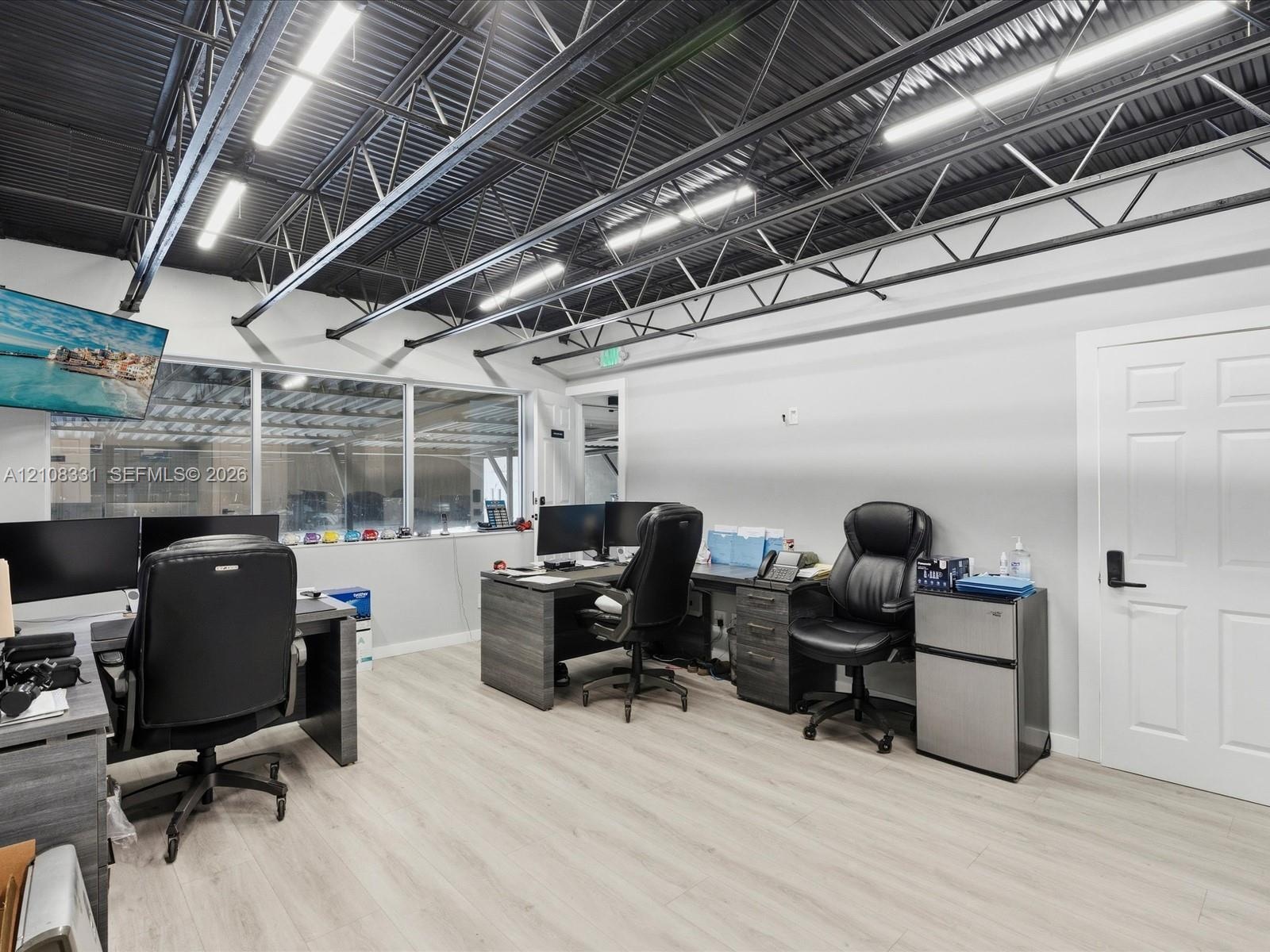 Industrial-style interior featuring an exposed black metal ceiling, linear LED light fixtures, wood-finish flooring, and expansive windows