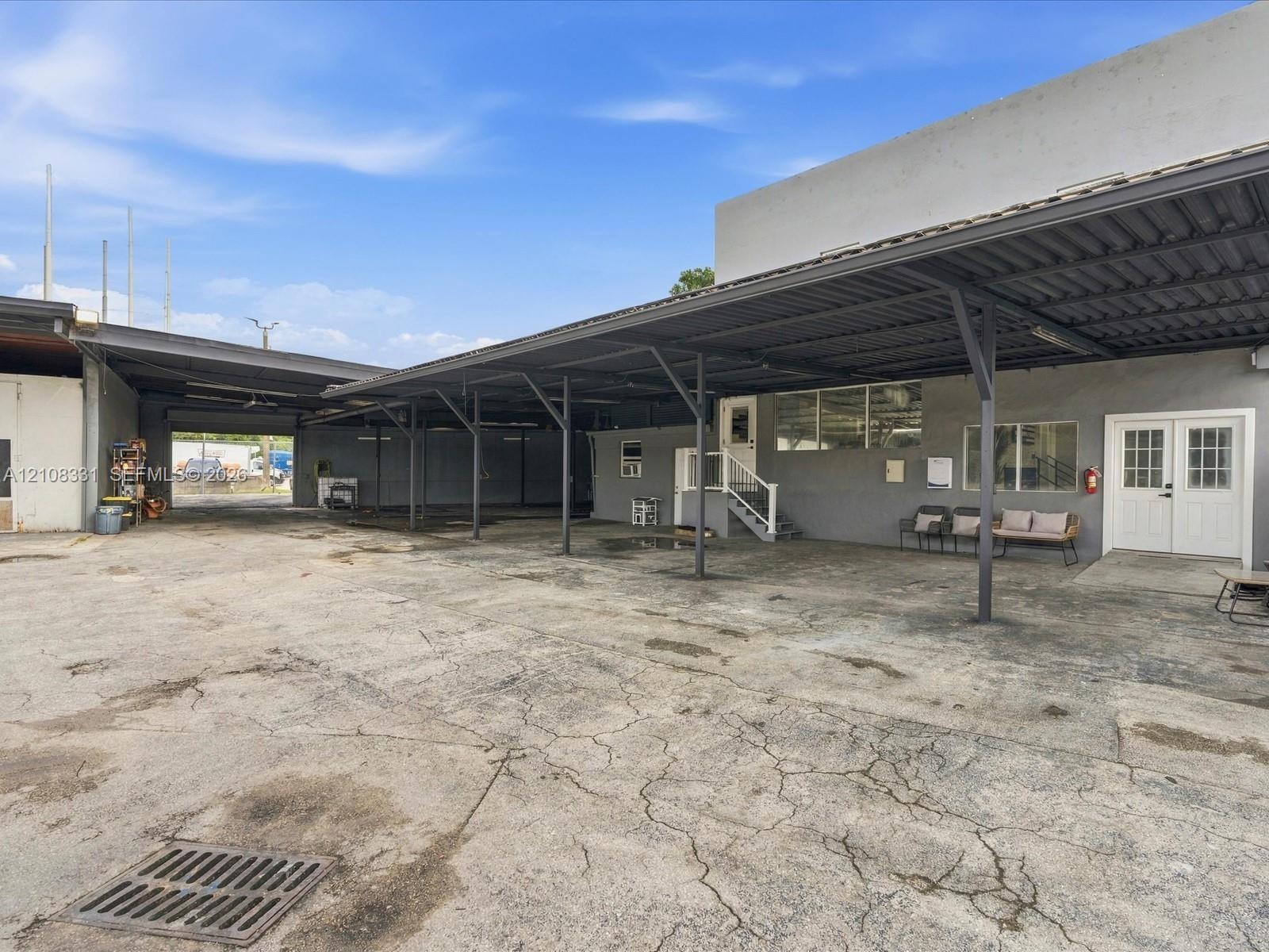 Expansive concrete exterior area featuring an integrated metal-framed canopy, dual-entry access points, a stepped platform entrance, and surface drain