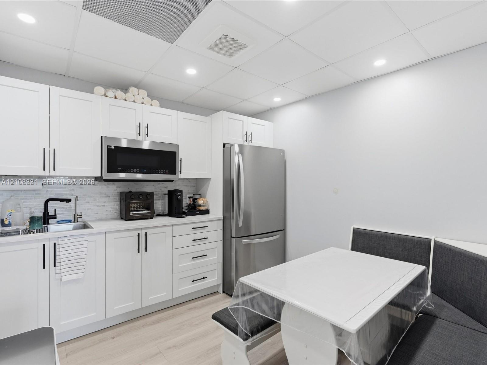 Kitchen featuring white shaker-style cabinetry, stainless steel appliances, a light-toned backsplash, recessed lighting, and wood-finish flooring