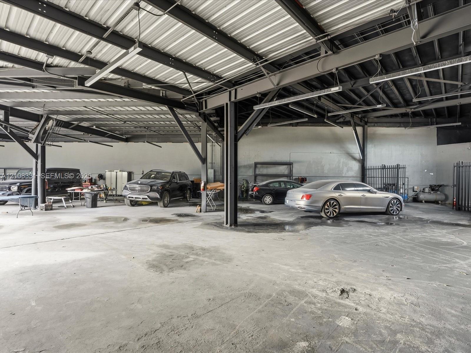 Expansive industrial-style garage featuring exposed steel beam framing, a high-clearance metal roof, concrete flooring, and overhead lighting fixtures