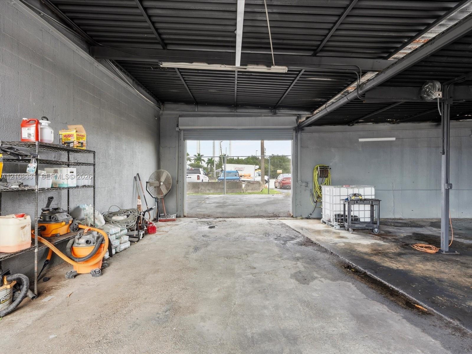 Open-bay warehouse structure featuring exposed metal ceiling joists, masonry walls, concrete flooring, and an oversized roll-up garage door