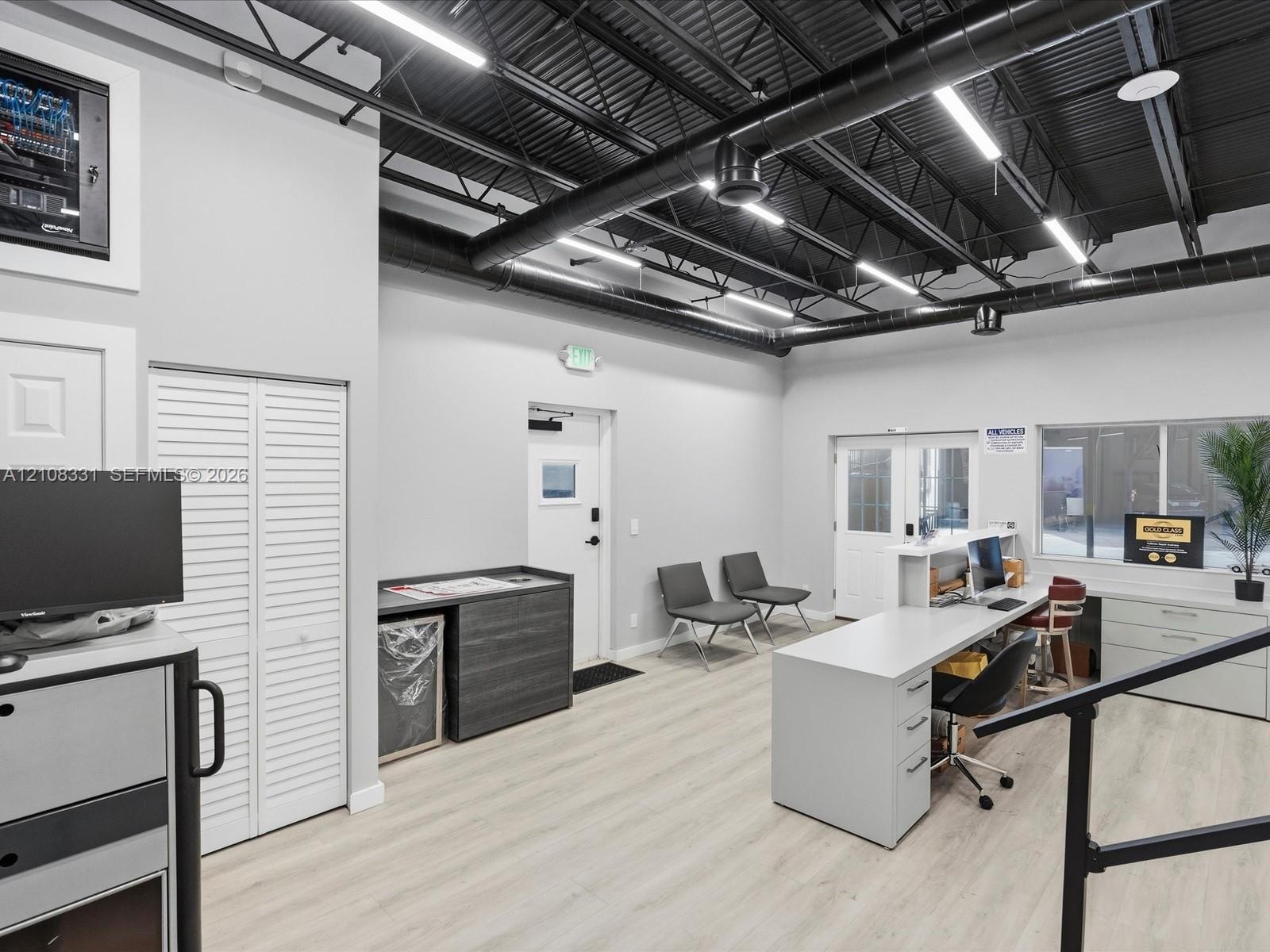 Open-concept workspace featuring industrial-style exposed black ceiling, wood-finish flooring, linear LED lighting, and built-in cabinetry with a mult