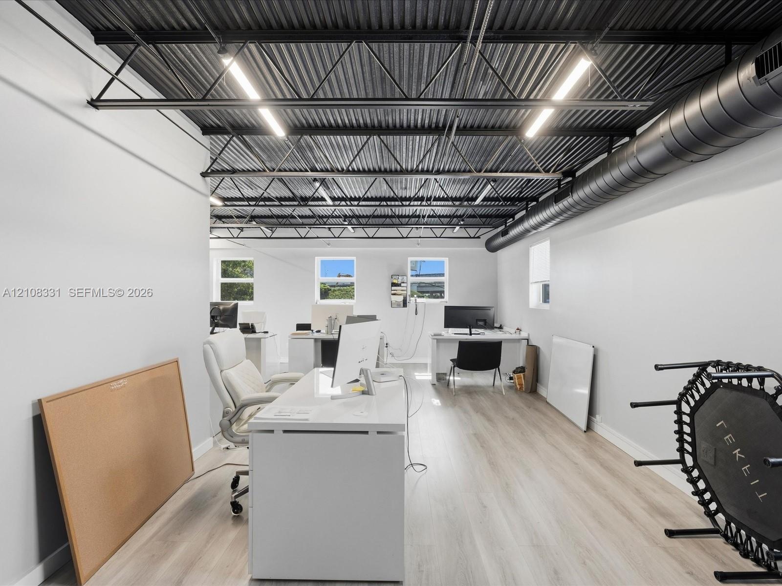 Industrial-style room featuring an exposed corrugated metal ceiling with dark steel trusses, linear LED lighting, and exposed circular ductwork, compl