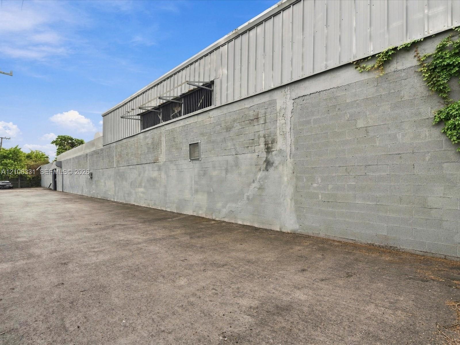 Industrial exterior featuring a concrete masonry unit wall, corrugated metal siding, and a paved asphalt surface