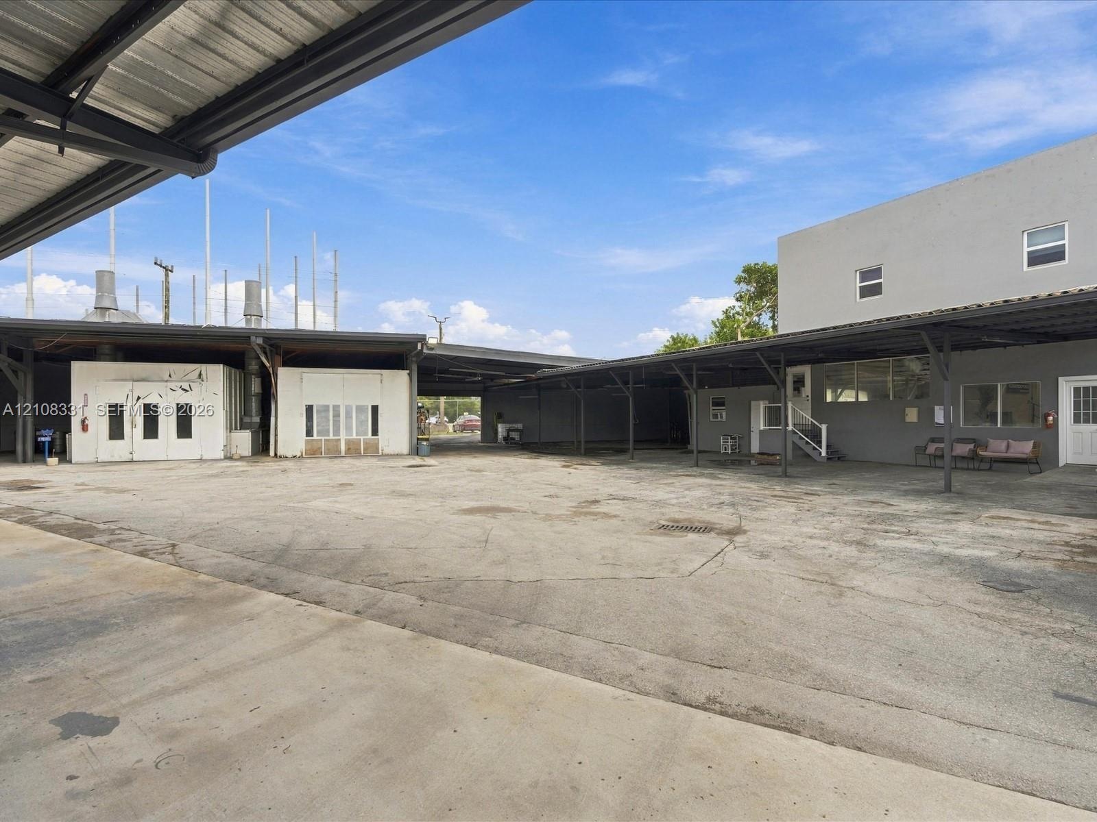 Expansive concrete exterior courtyard featuring extensive metal-framed covered parking, multi-level building structures, and industrial-style exterior