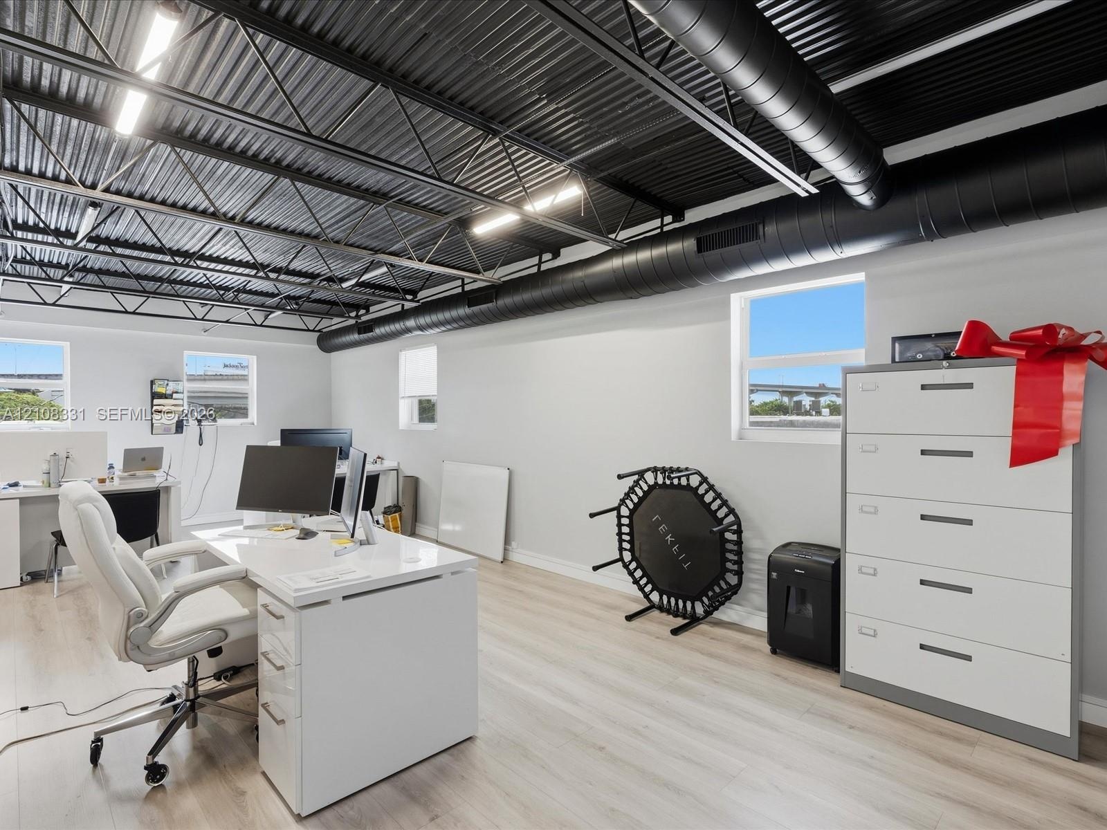 Open-concept room featuring a corrugated metal ceiling with exposed black industrial ducting, wood-finish flooring, and multiple exterior-facing windo