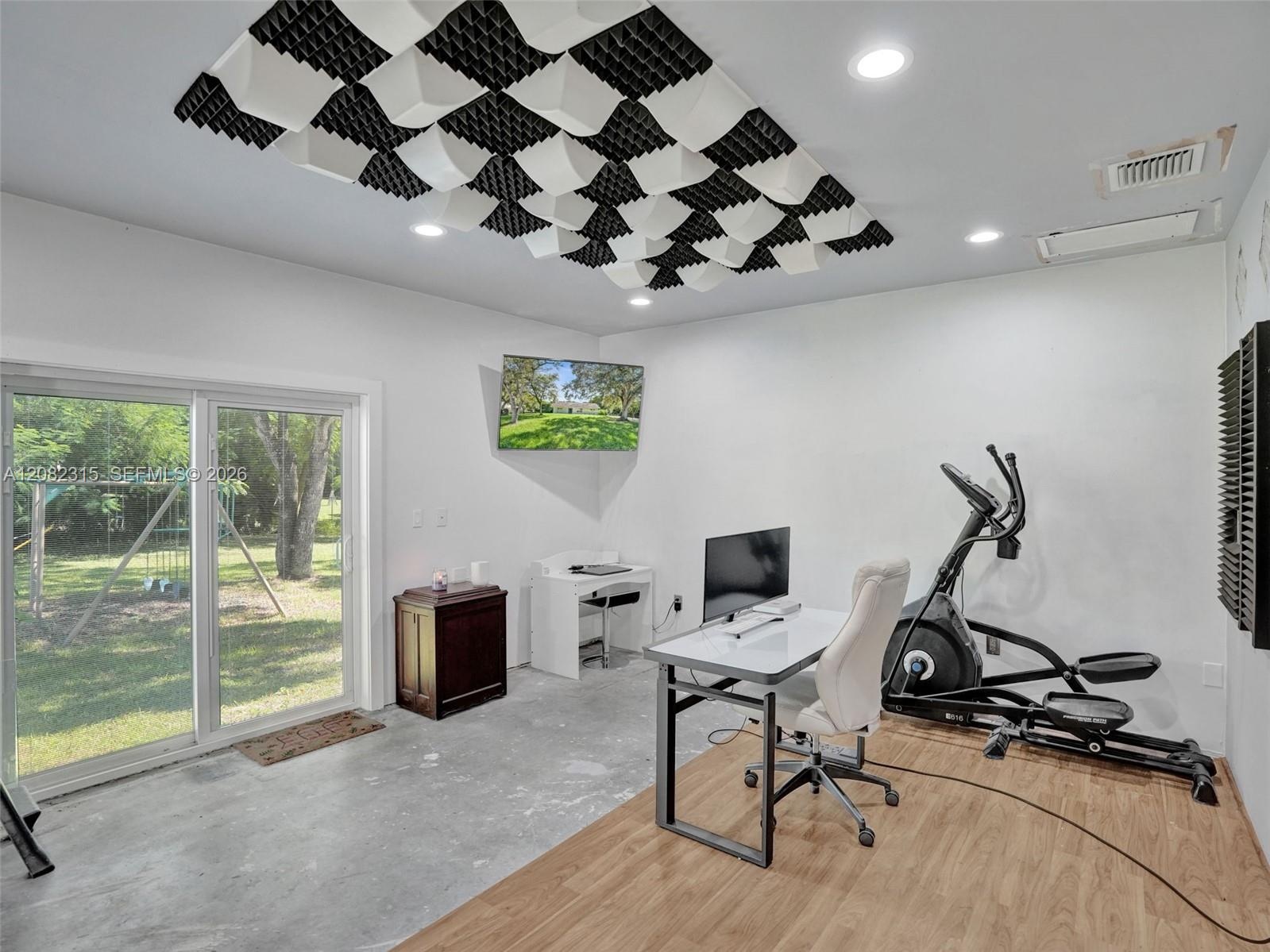 Interior space featuring wood-finish flooring, concrete flooring, sound-dampening ceiling panels, recessed lighting, and a sliding glass door