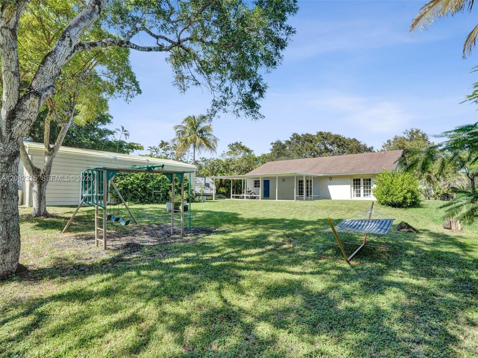 Expansive backyard featuring a sprawling lawn, mature trees, a detached storage structure, and a covered rear patio
