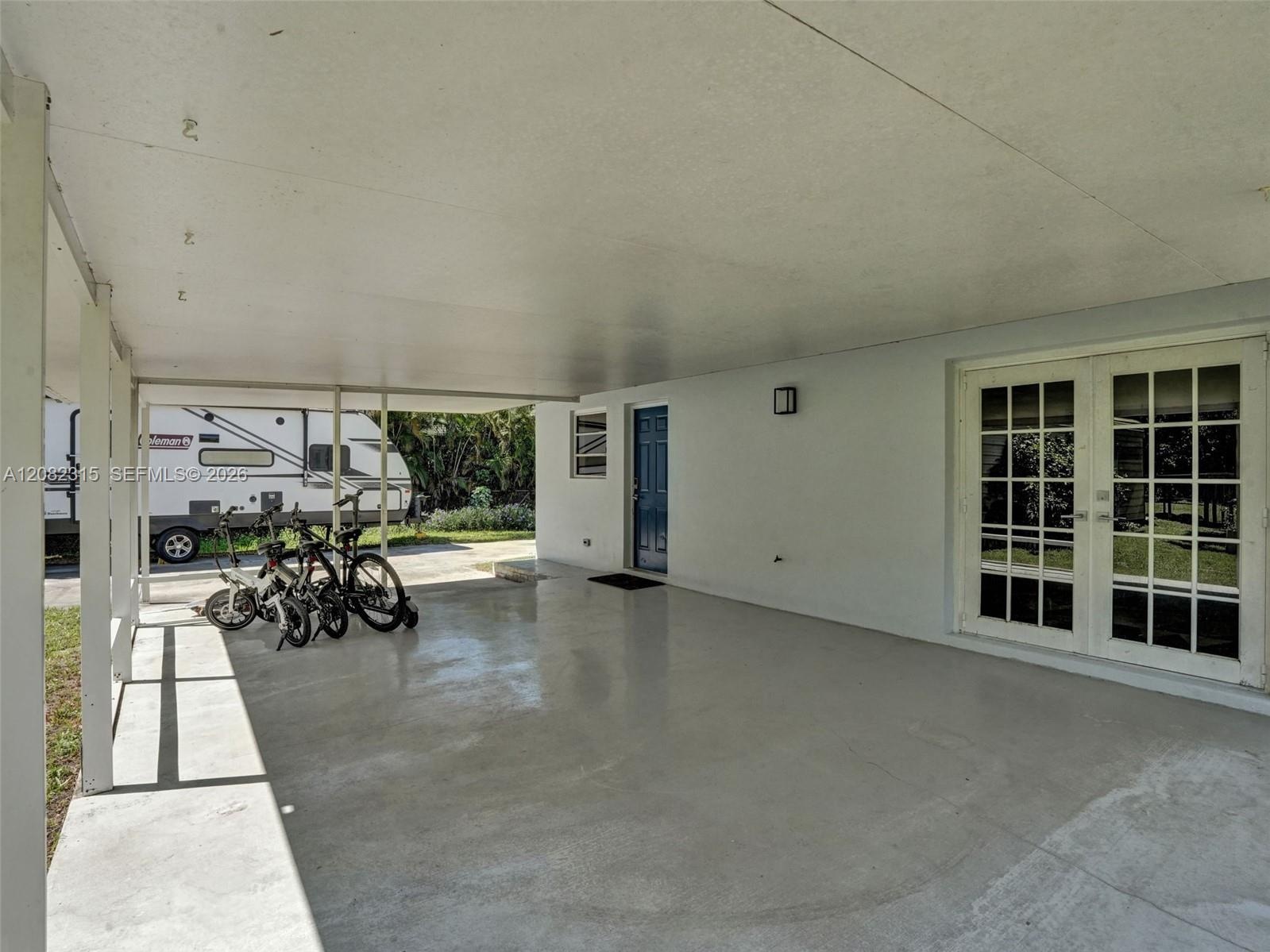 Covered carport featuring a smooth concrete floor, white support pillars, and glass-paned double doors
