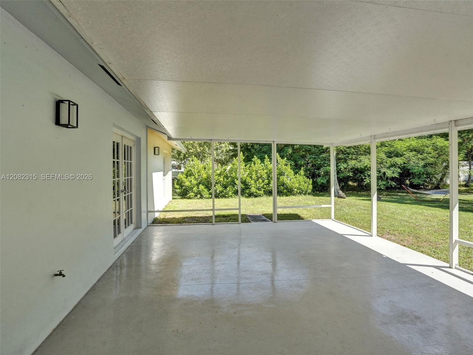 Screened-in patio featuring a solid roof, concrete flooring, exterior wall-mounted lighting, and double-door access