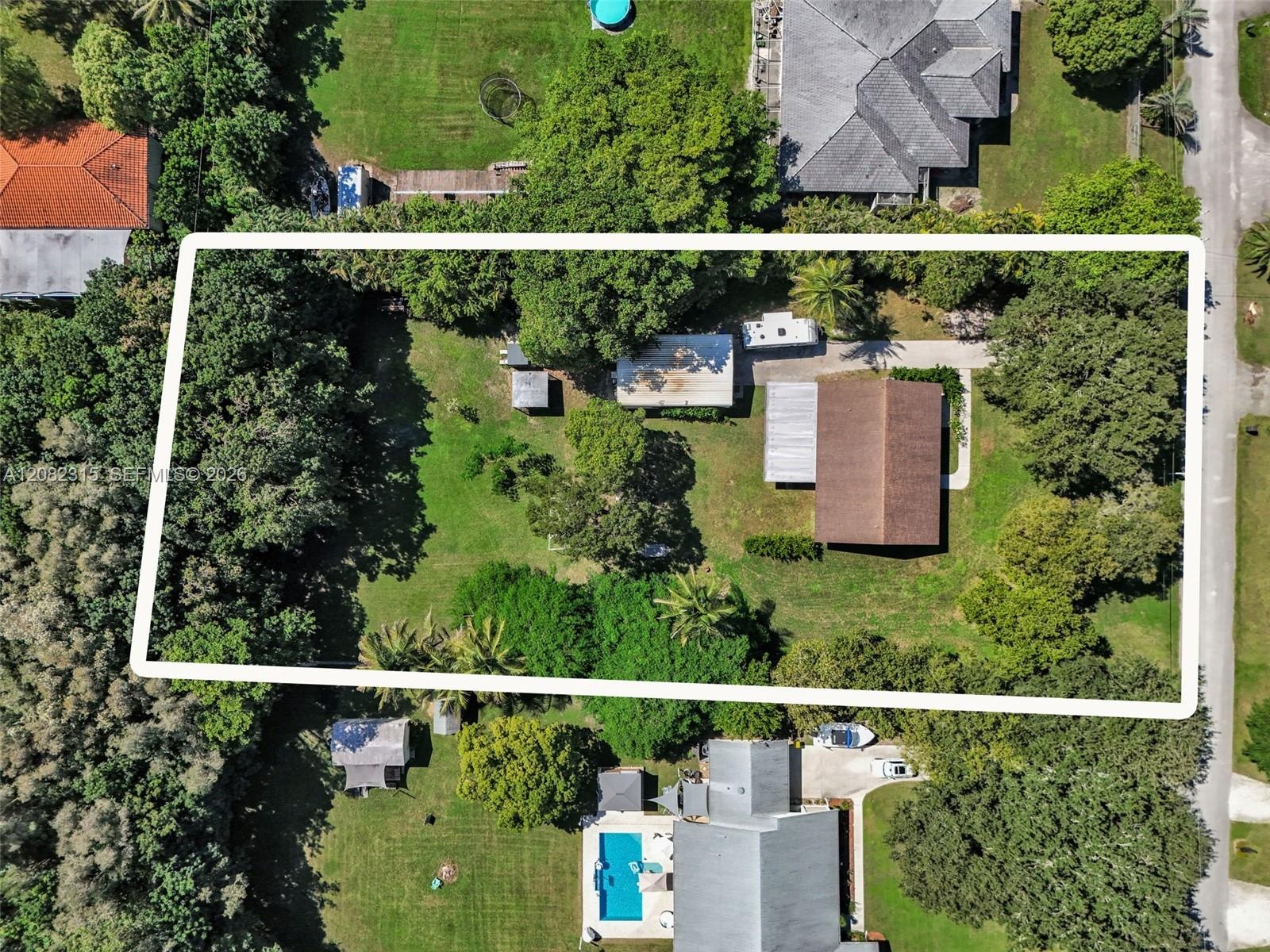 Aerial view of a sprawling lot featuring mature trees, substantial lawn area, a detached structure, and an asphalt driveway