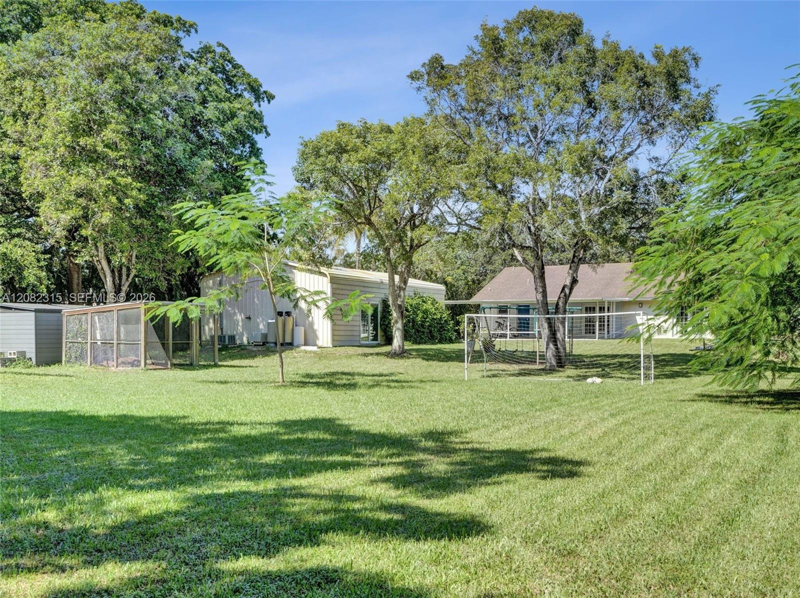 Expansive lot featuring mature trees, a metal-sided detached structure, and a fenced enclosure