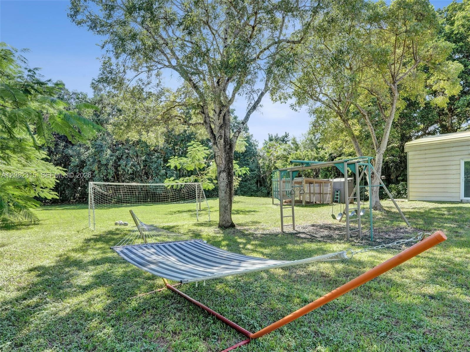 Expansive backyard featuring a large grass lawn, mature shade trees, and perimeter foliage