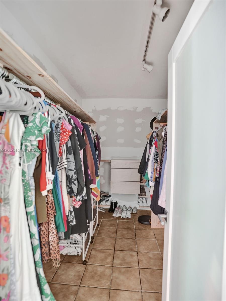 Walk-in storage space featuring ceramic tile flooring, built-in shelving, a wall-mounted chest of drawers, and adjustable track lighting