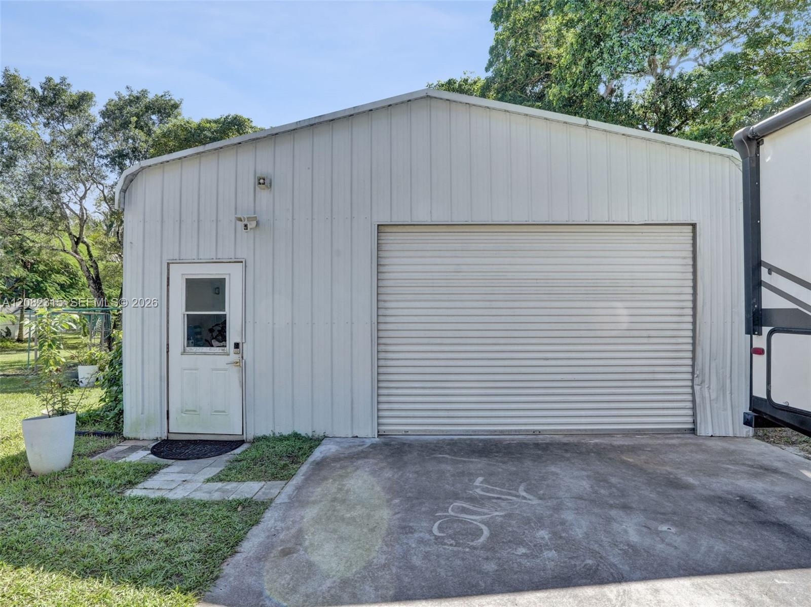 Detached metal workshop featuring a roll-up garage door, separate pedestrian entry, and a concrete apron