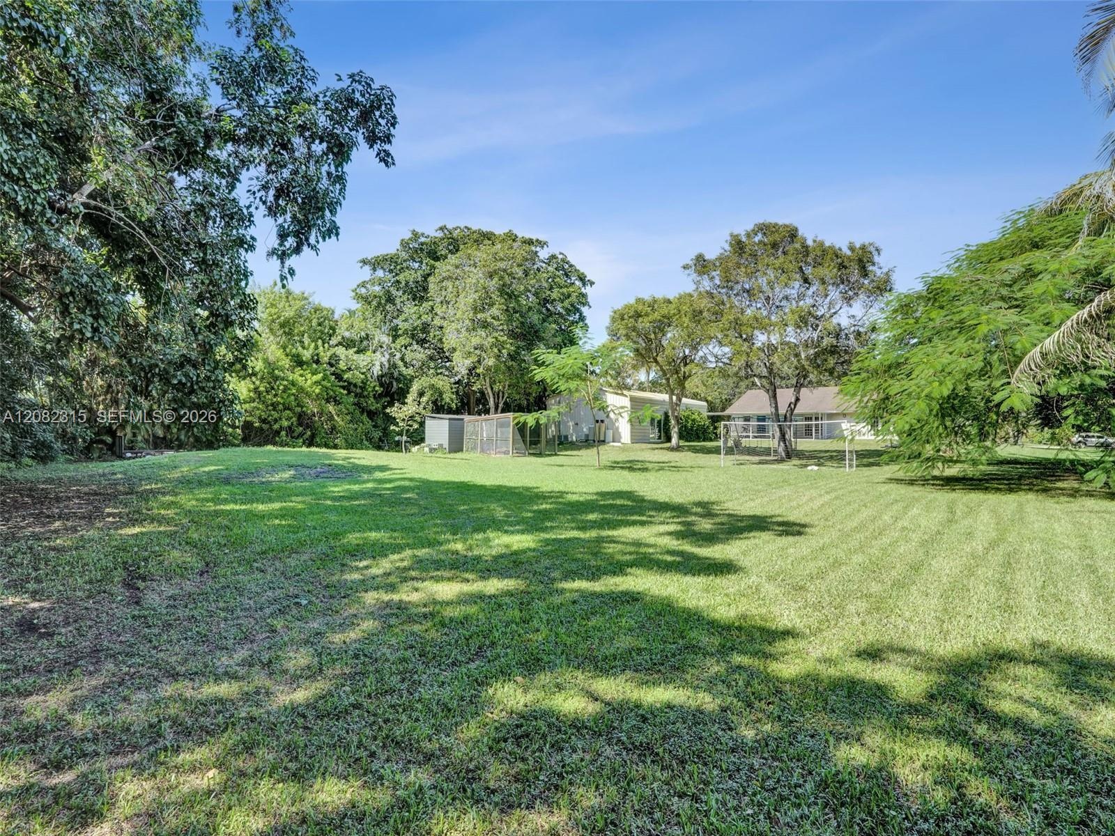 Expansive backyard featuring a manicured lawn, mature trees, and perimeter vegetation