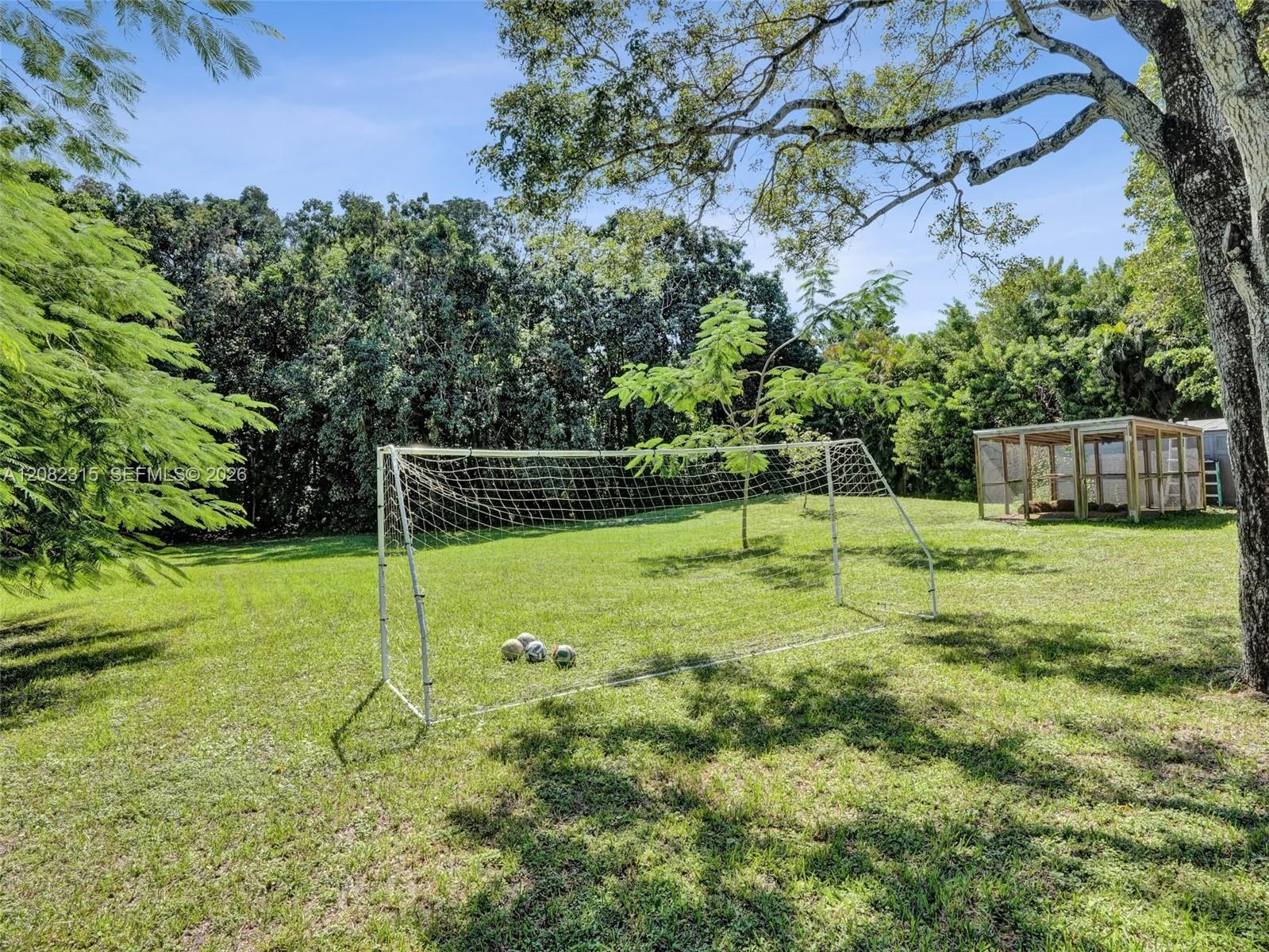 Expansive lawn area featuring mature trees and a detached wood-frame structure with wire mesh enclosure
