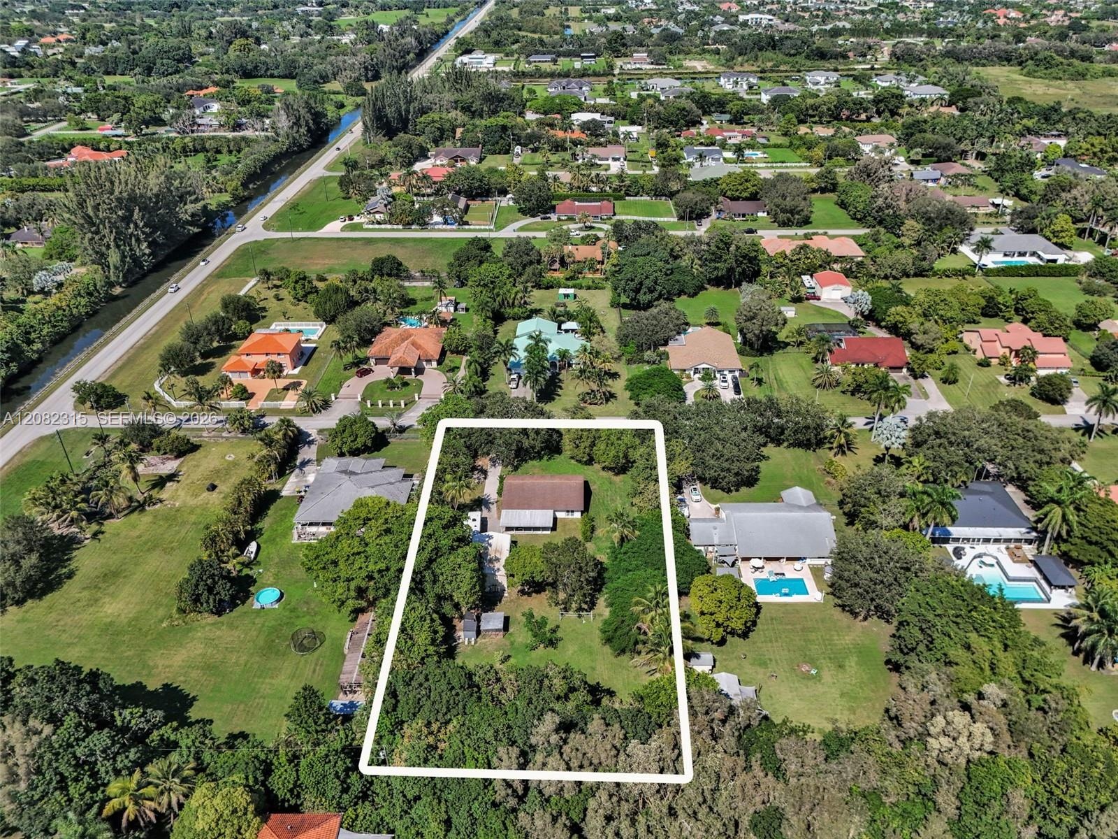 Aerial perspective of a multi-acre property featuring mature tree canopy, extensive open lawn space, and a paved driveway