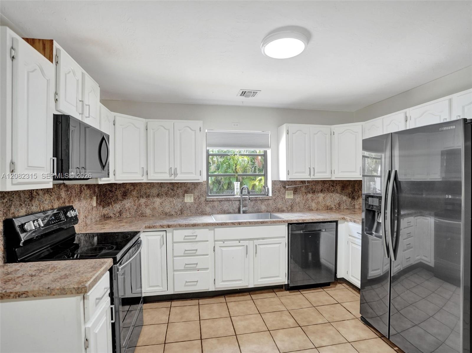 Kitchen featuring white cabinetry, solid-surface countertops, tile flooring, and integrated black appliances