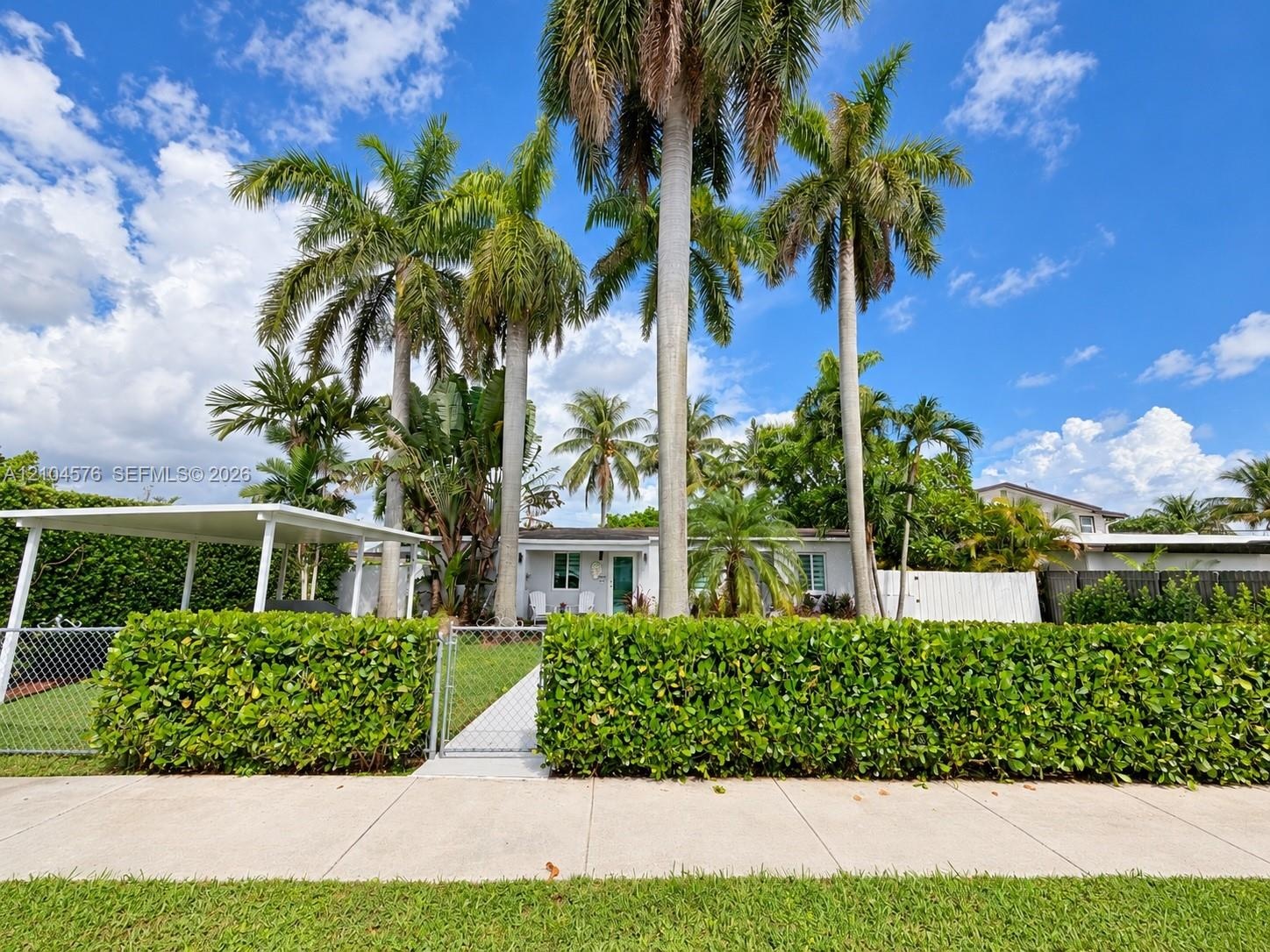 Covered front porch featuring large-format tile flooring, porcelain-tiled walkway, manicured landscaping, and mature palm trees