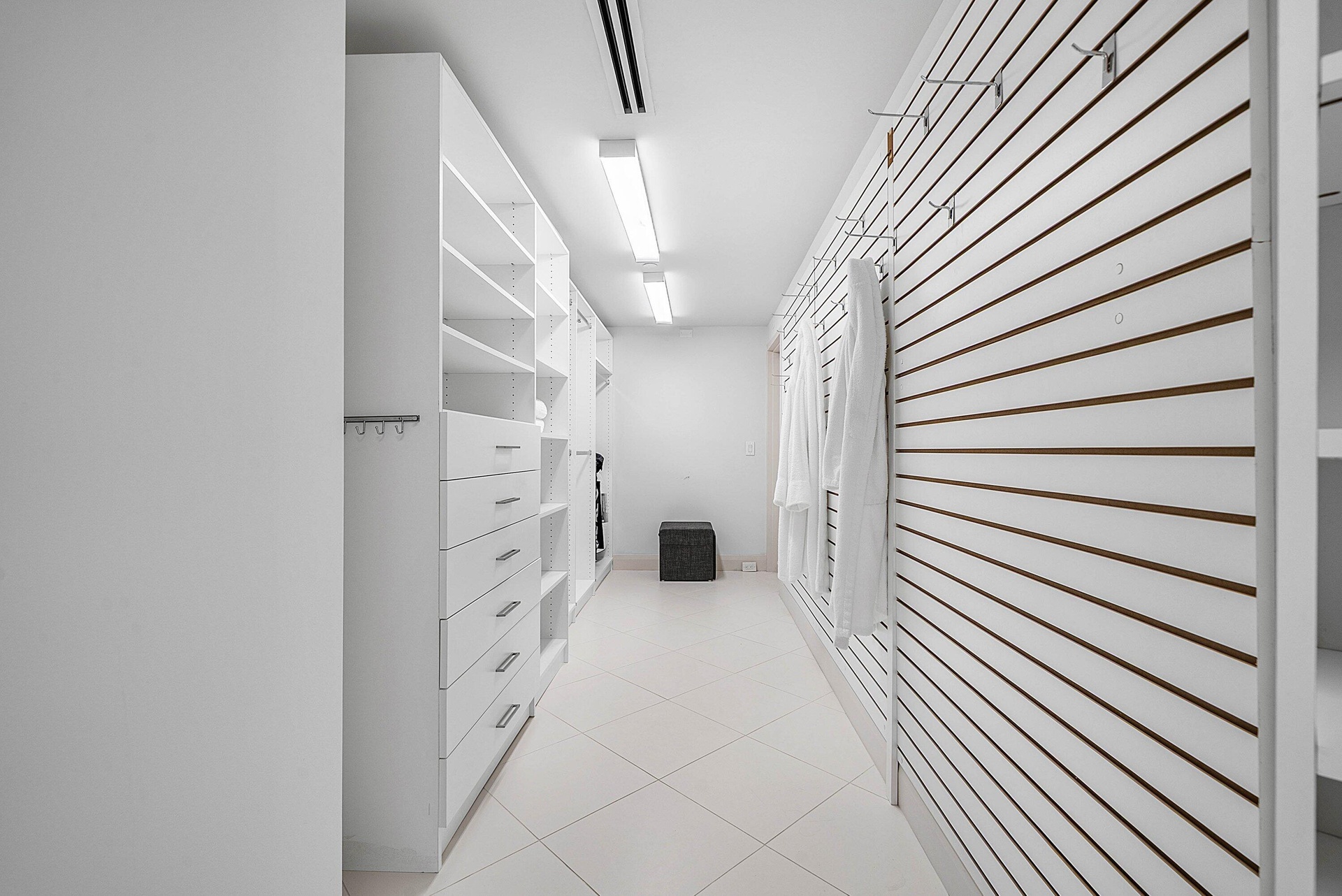 Walk-in closet featuring white built-in cabinetry with integrated drawers, slat-wall organizational system with adjustable hooks, tile flooring, and l